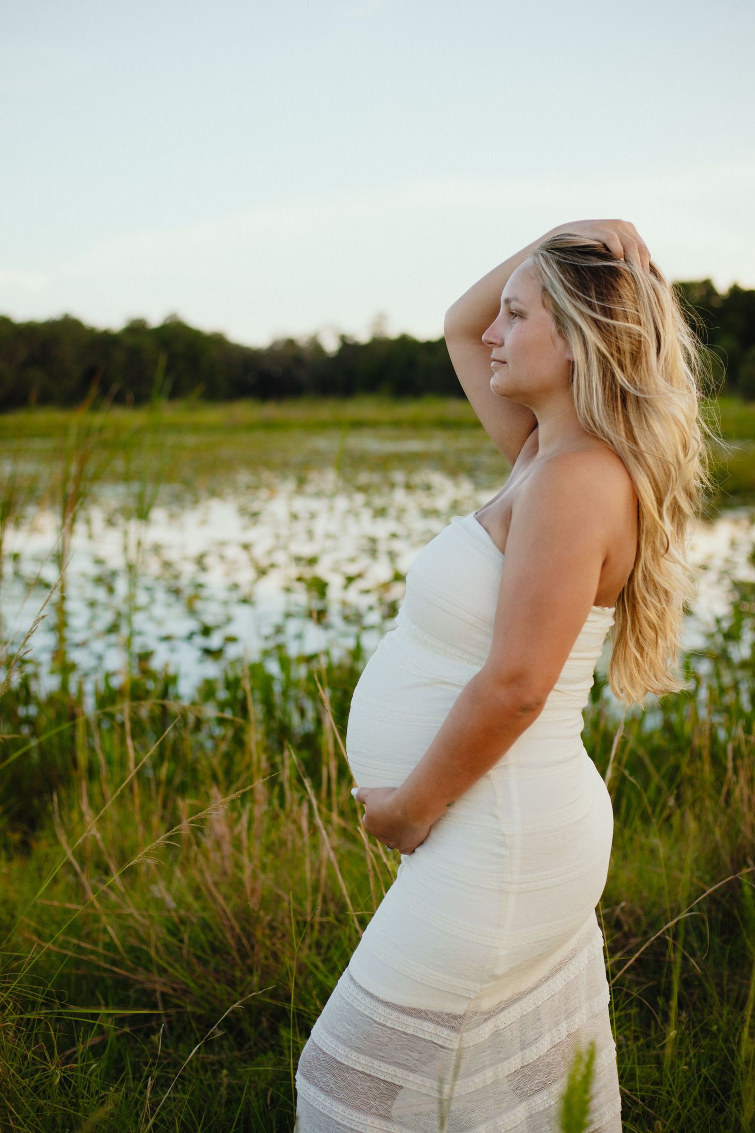 Ethereal maternity portraits in a sunlit field with flowing white dress.