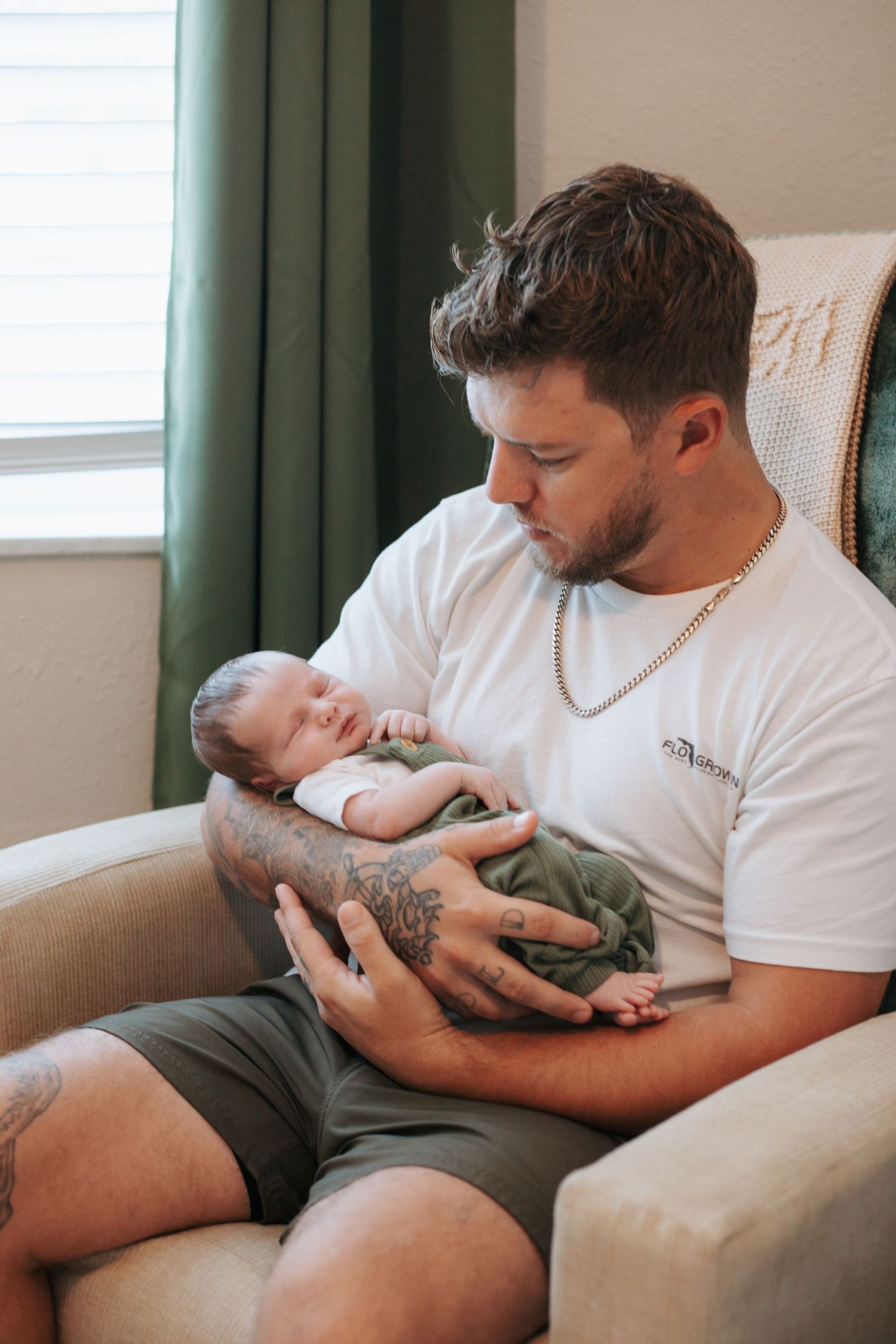 A tender moment as a parent in a white t-shirt cradles their sleeping newborn baby in a cozy armchair.