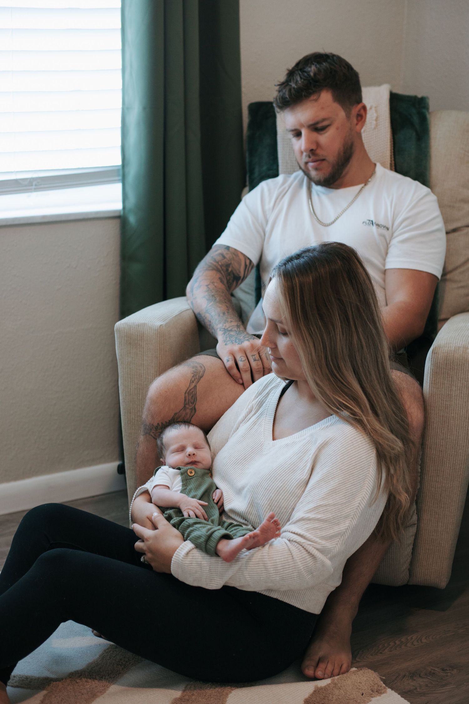 A family relaxes together on a couch while looking at a small infant in their arms.