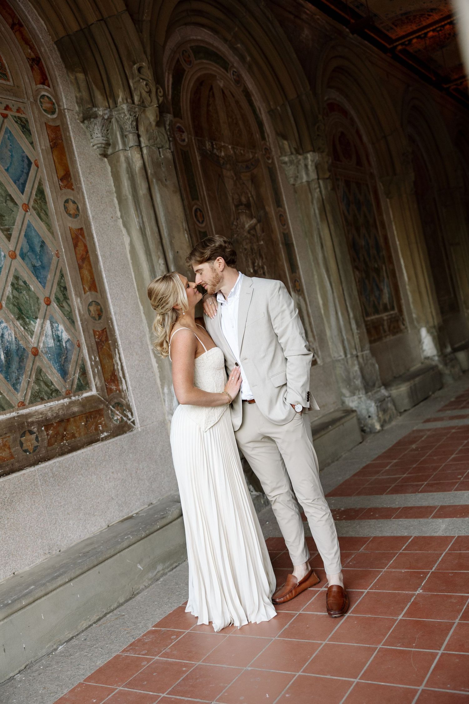 Central Park New York Photography - Couple sharing romantic moment in ornate frescoed archway, bride in white gown and groom in beige suit.