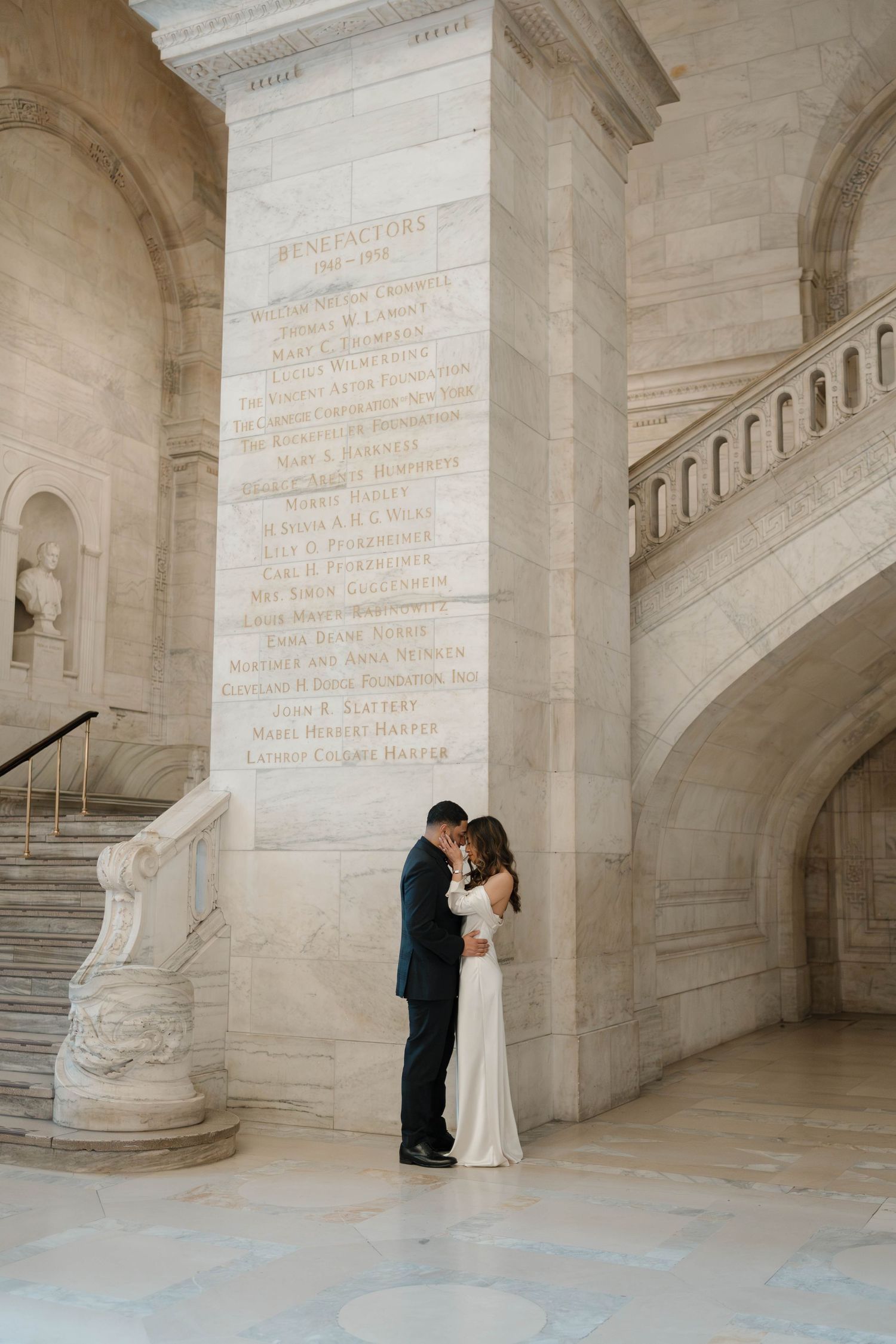 Couple embracing beside an engraved marble column near the grand staircase of the New York Public Library.