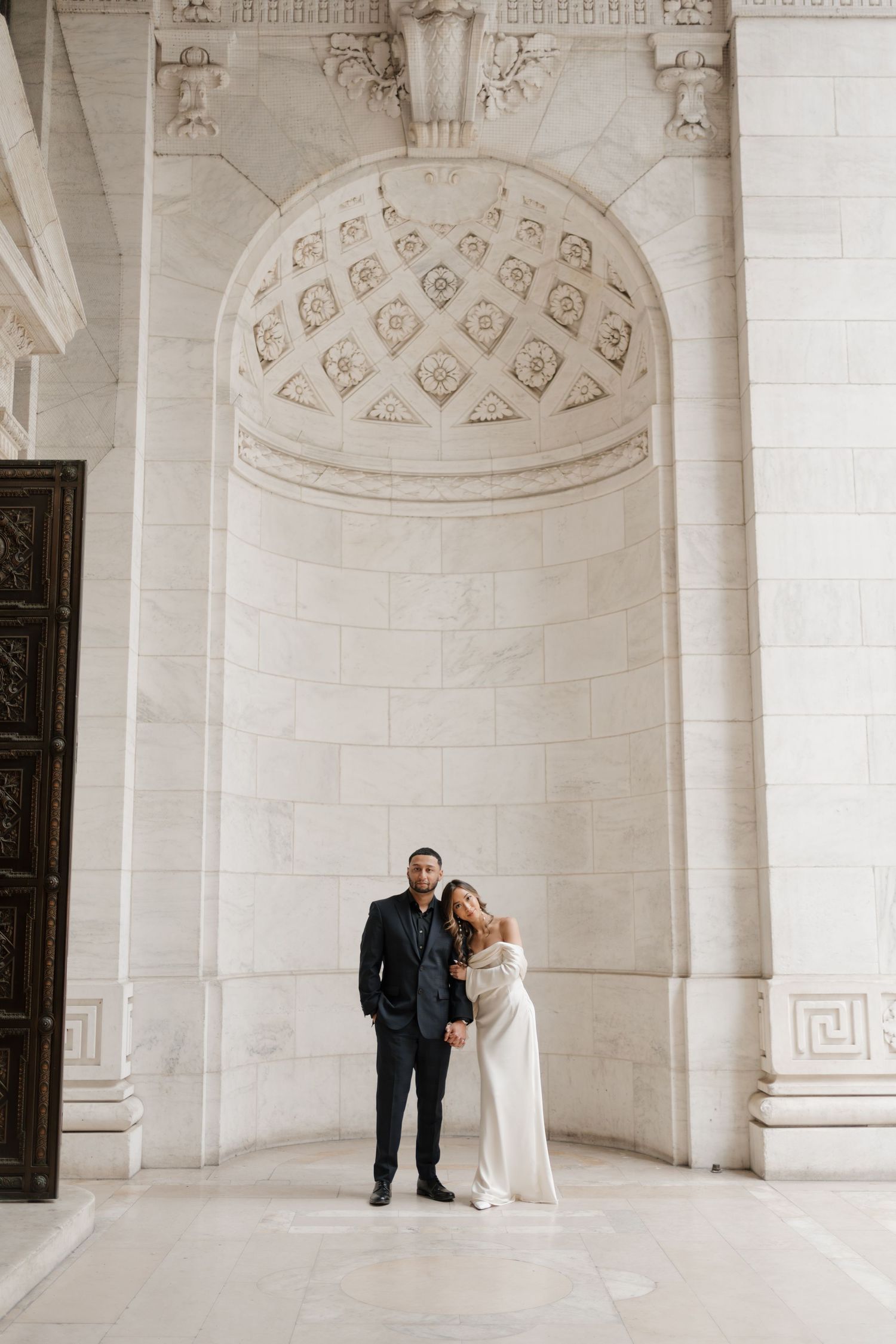 Wedding couple embracing under decorative stone archway with intricate carved details.