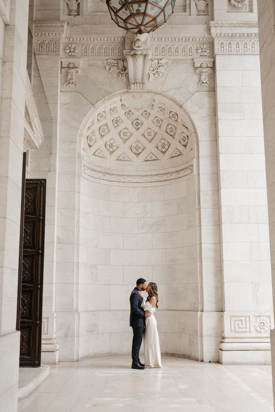 Couple sharing a romantic embrace in an elegant marble archway of the New York Public Library.