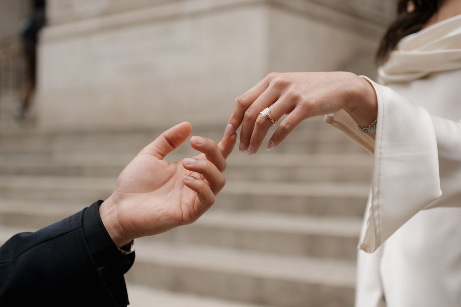 Close-up of couple touching fingertips, showcasing engagement ring on bride's hand.