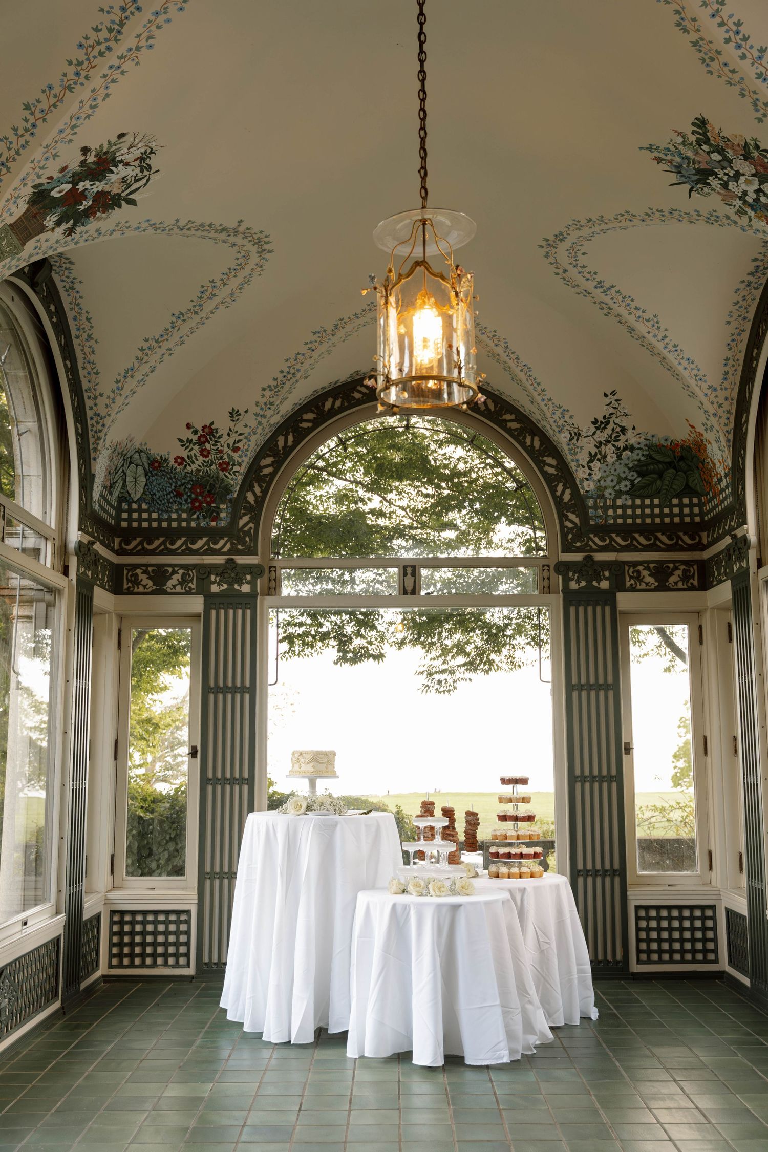 Elegant wedding reception setup in a ornate gazebo with white tablecloths and floral ceiling murals.