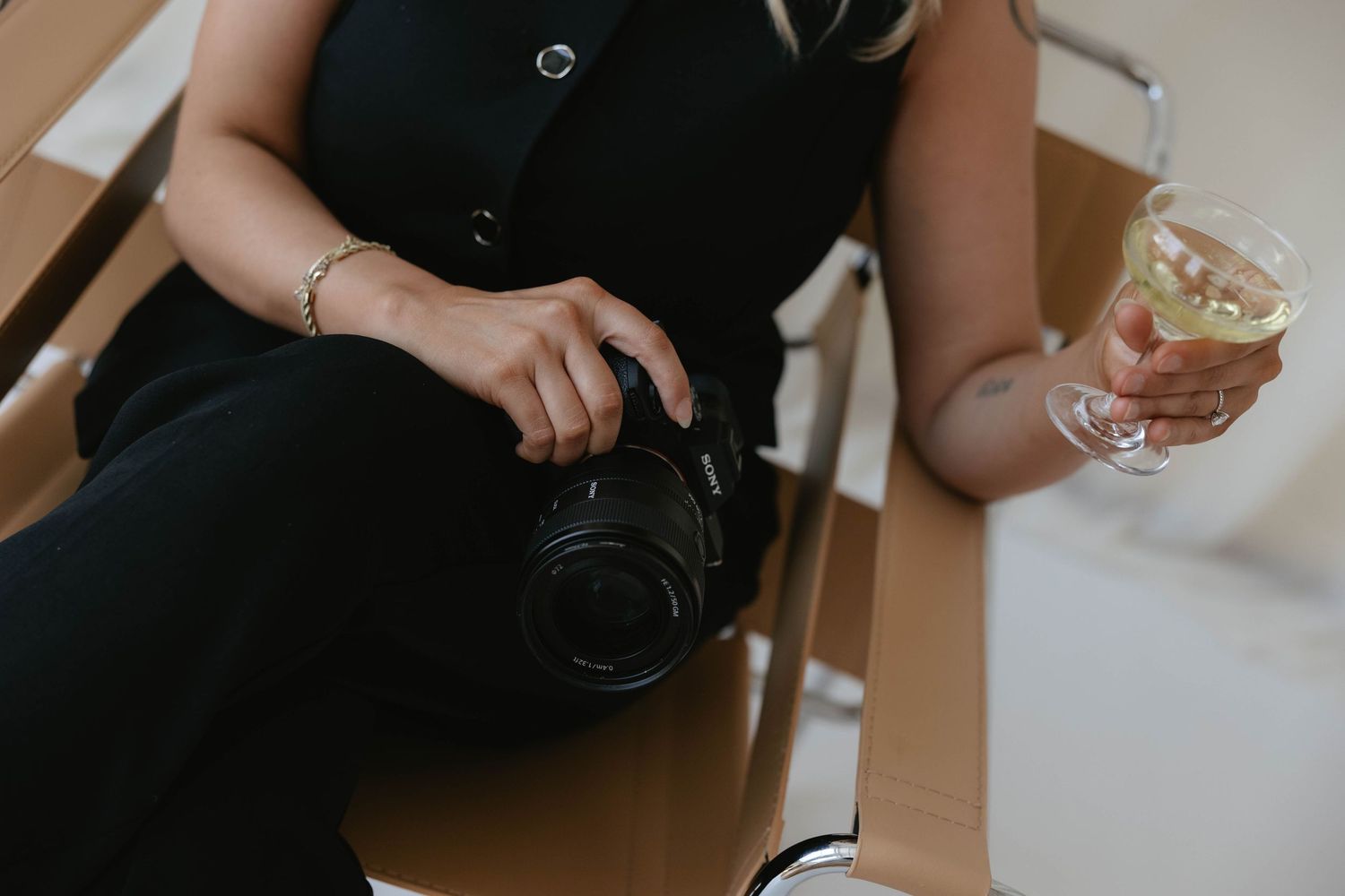 Close-up of wedding photographer holding a Canon DSLR camera and a stemmed glass with a citrus garnish.