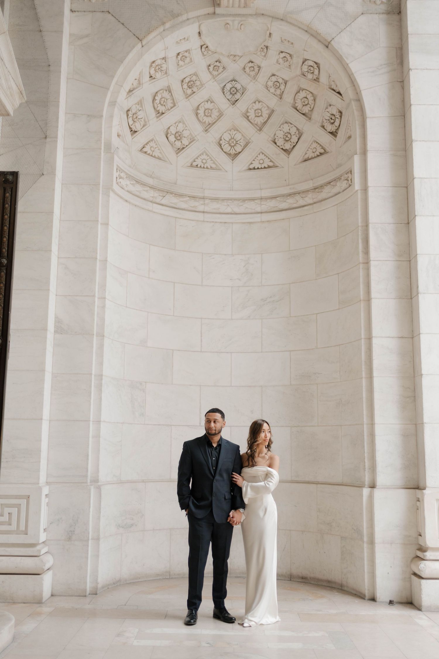 Bride and groom posing beneath an ornate marble arch at the New York Public Library.