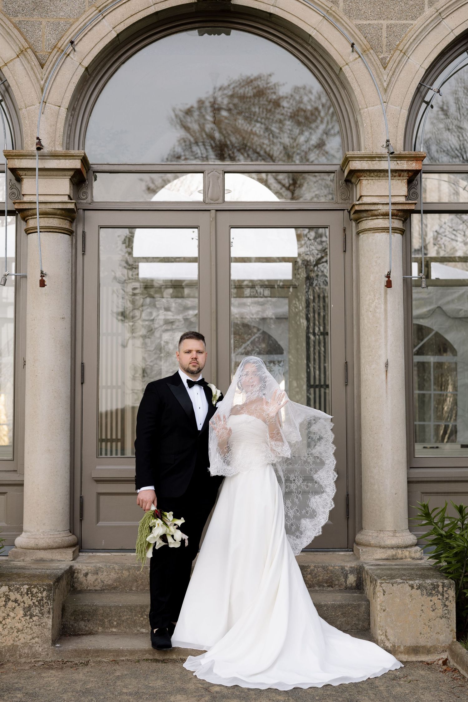 Eolia Mansion at Harkness Memorial Park - Bride and groom posing grand arched windows, bride wearing flowing lace veil and white gown.