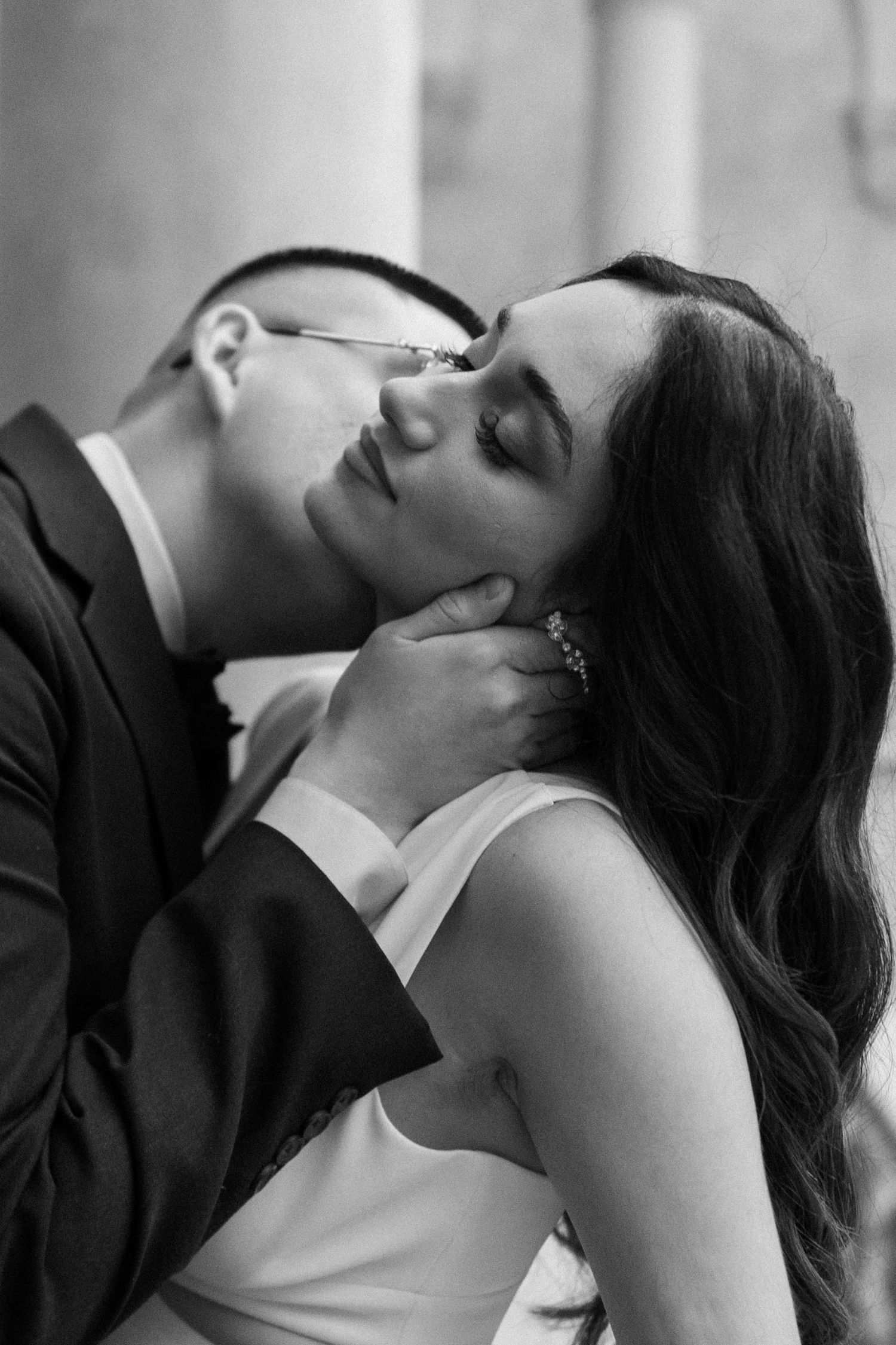 Black and white intimate moment of groom tenderly kissing bride's cheek while cradling her face.