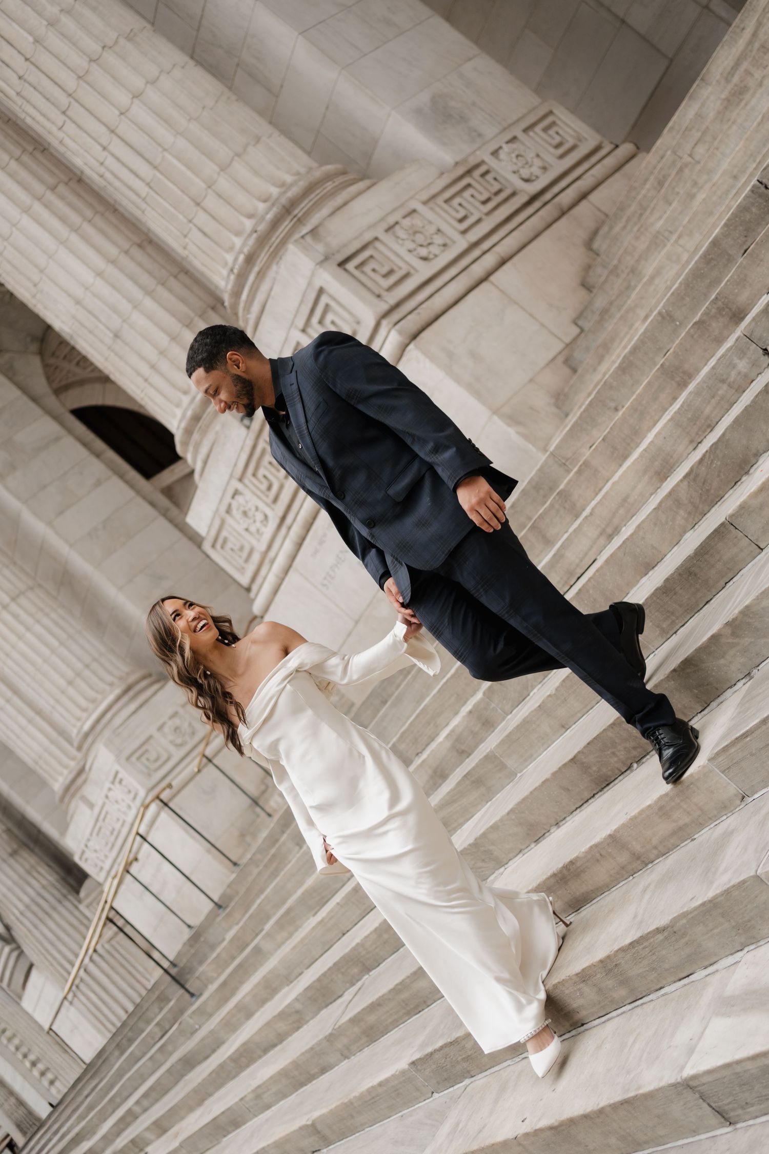 Low angle view of bride and groom holding hands on ornate marble staircase.