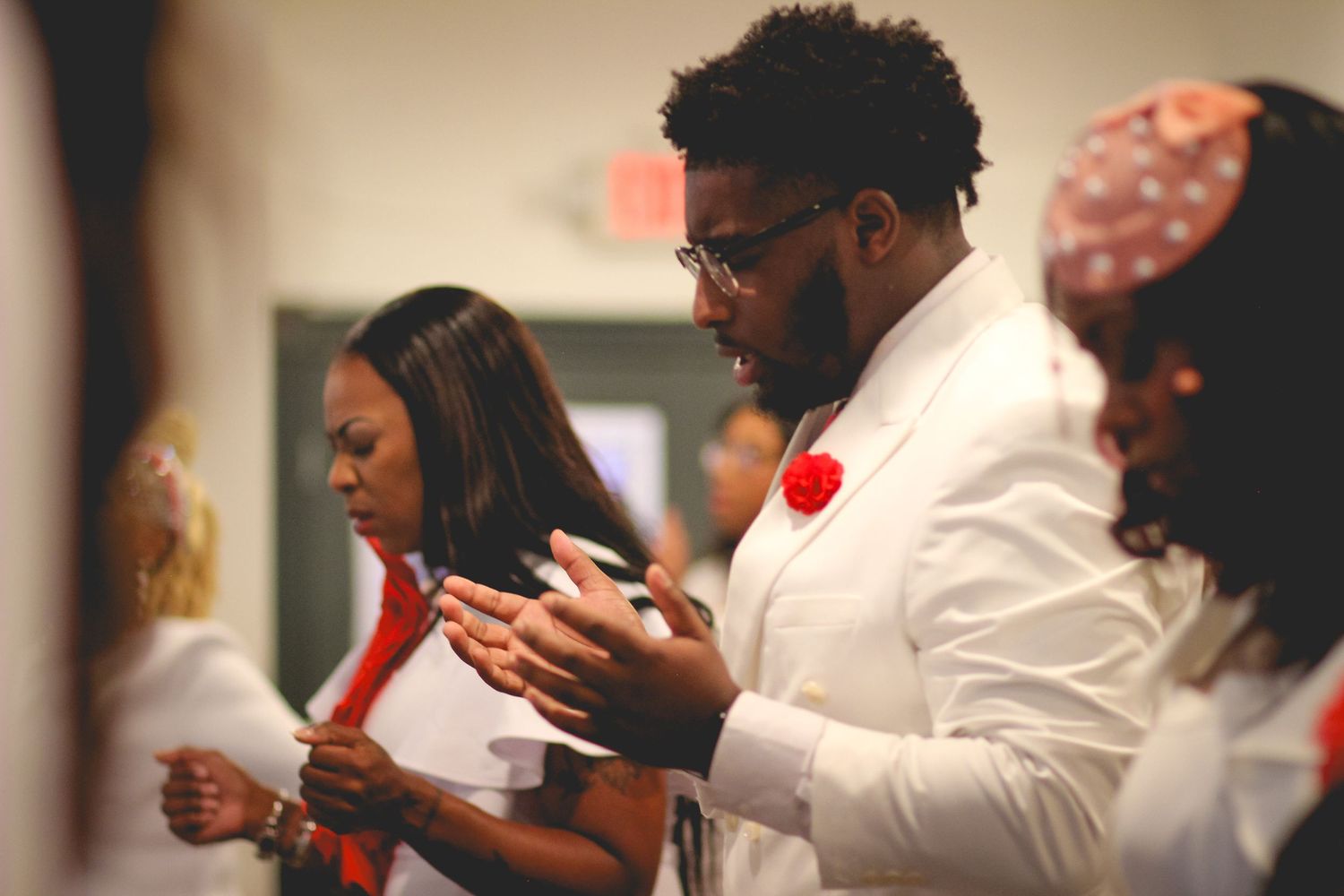A group of people in white shirts stand together while looking down at their mobile phones during an event.