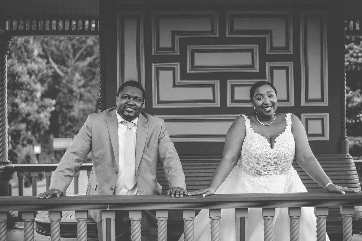 A black and white photo of a happy couple on their wedding day standing on a porch with a decorative door behind them.