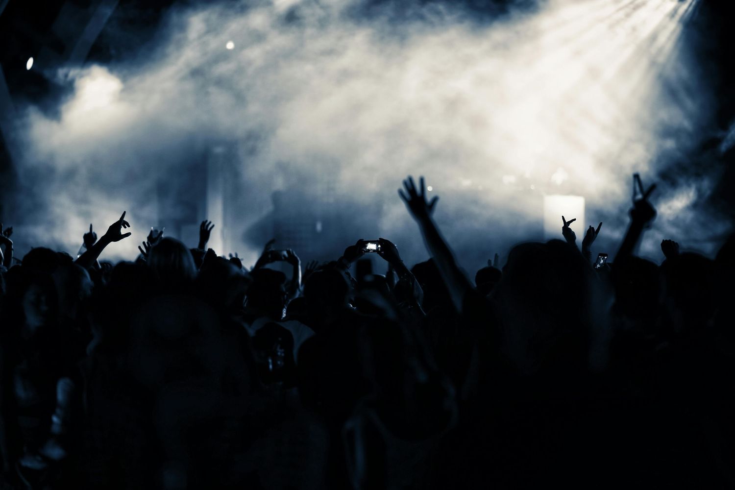 Dramatic concert crowd silhouette against cloudy sky with stage lighting.