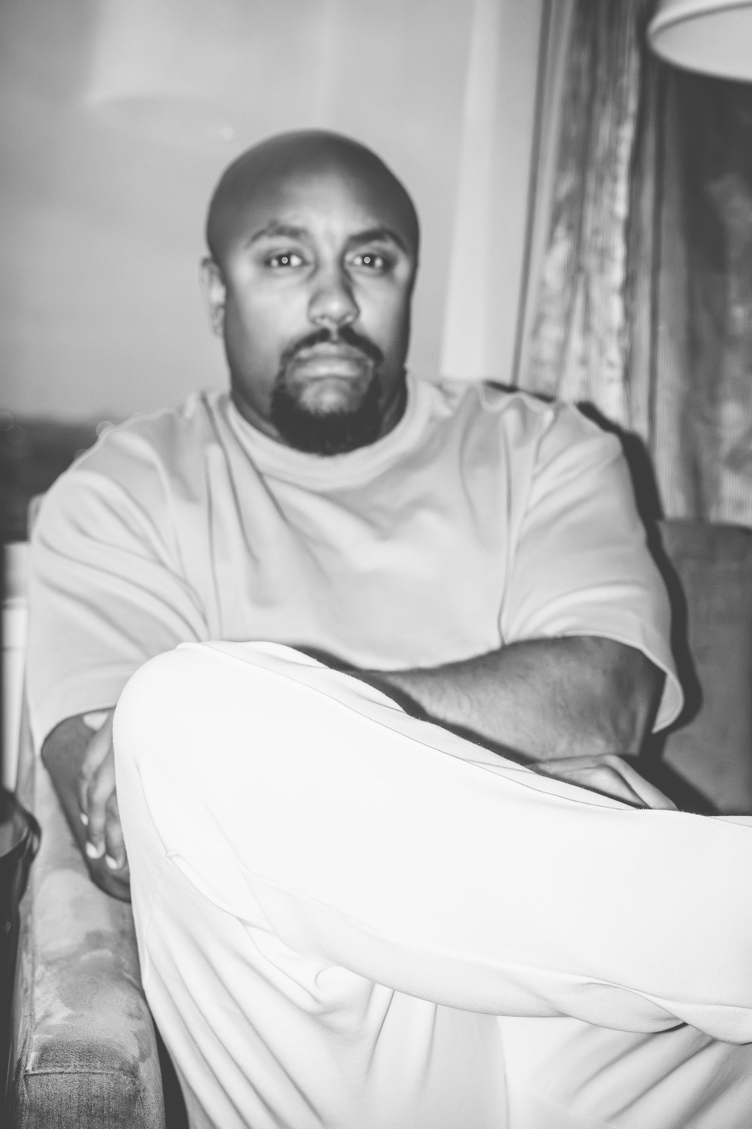 Person in white sweater sits casually on couch in black and white portrait.