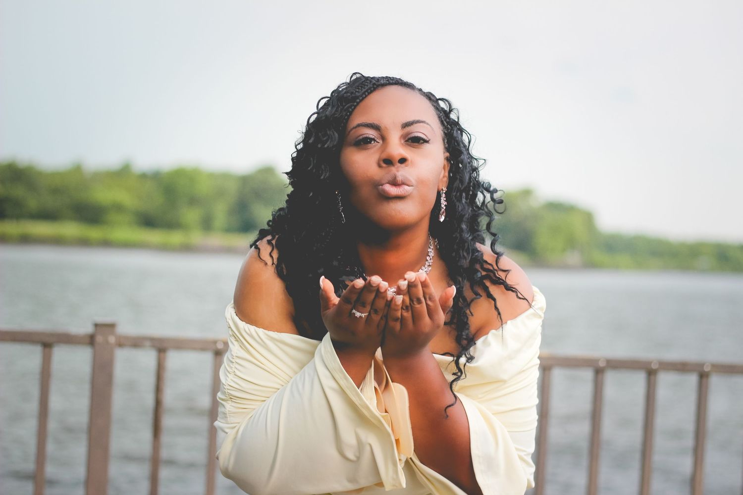 A series of romantic outdoor portraits showing someone in white blowing kisses by a waterfront wooden railing.