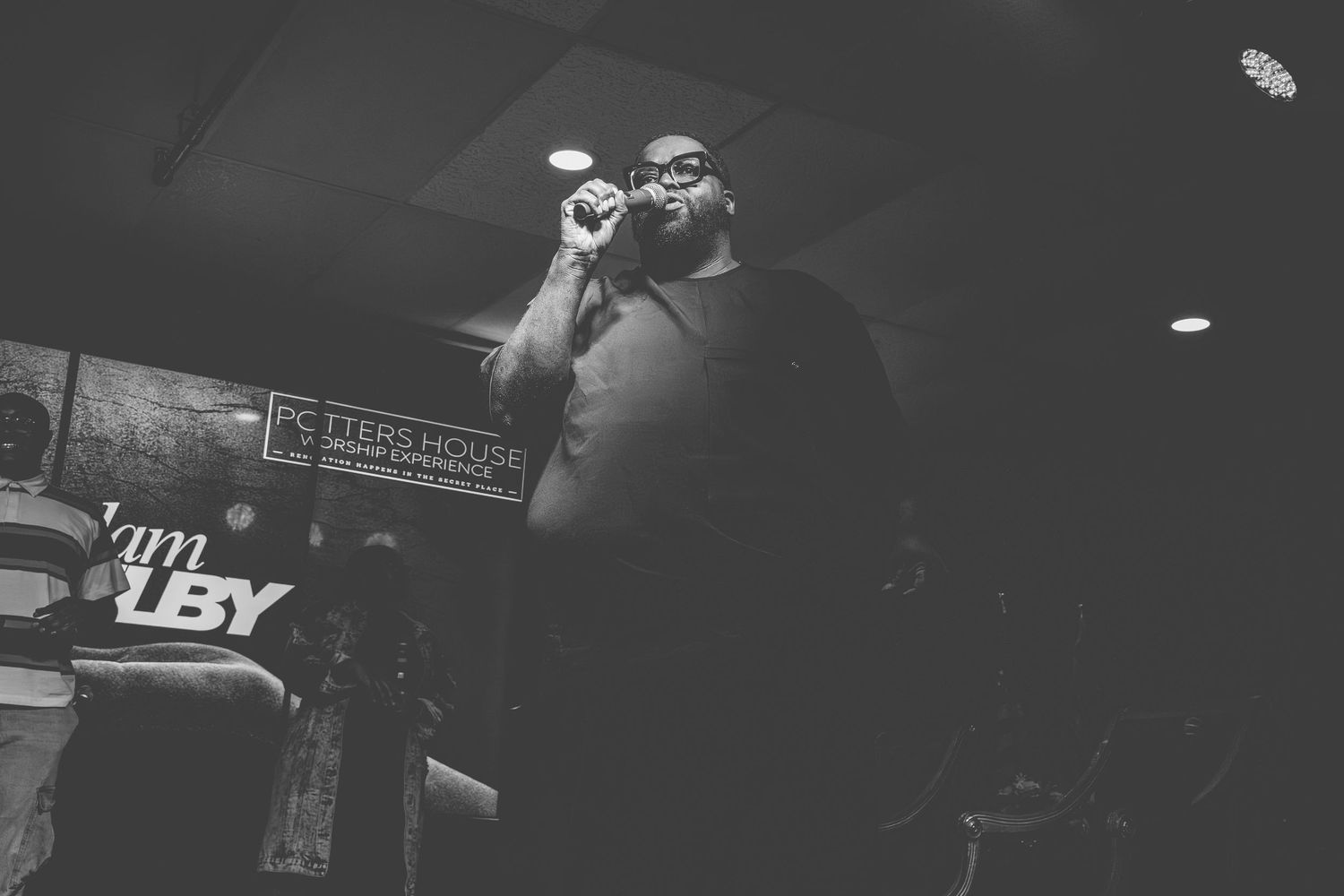 Black and white photo of a performer on stage with microphone at a music venue.