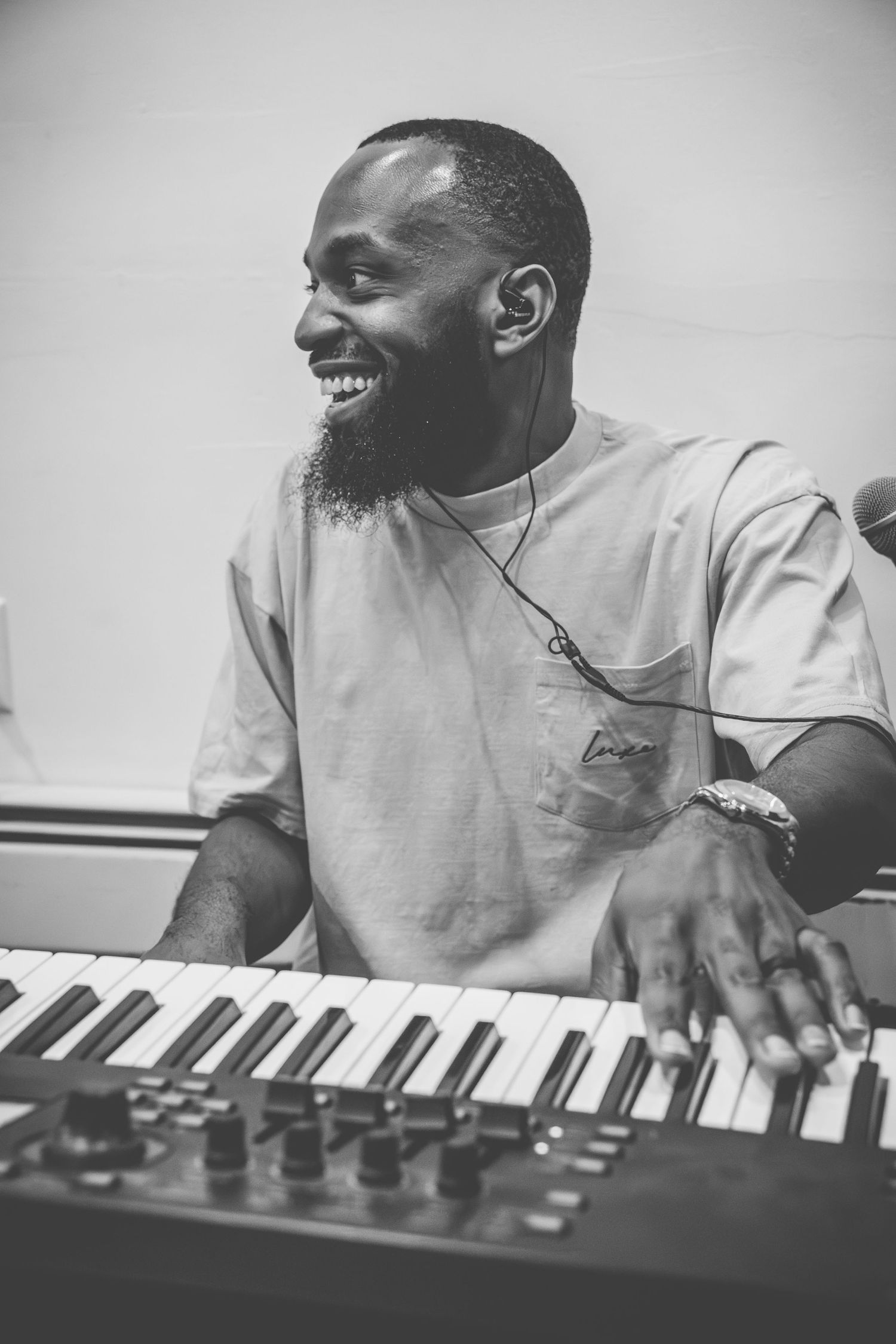 A musician plays a keyboard while smiling in a black and white candid photo.