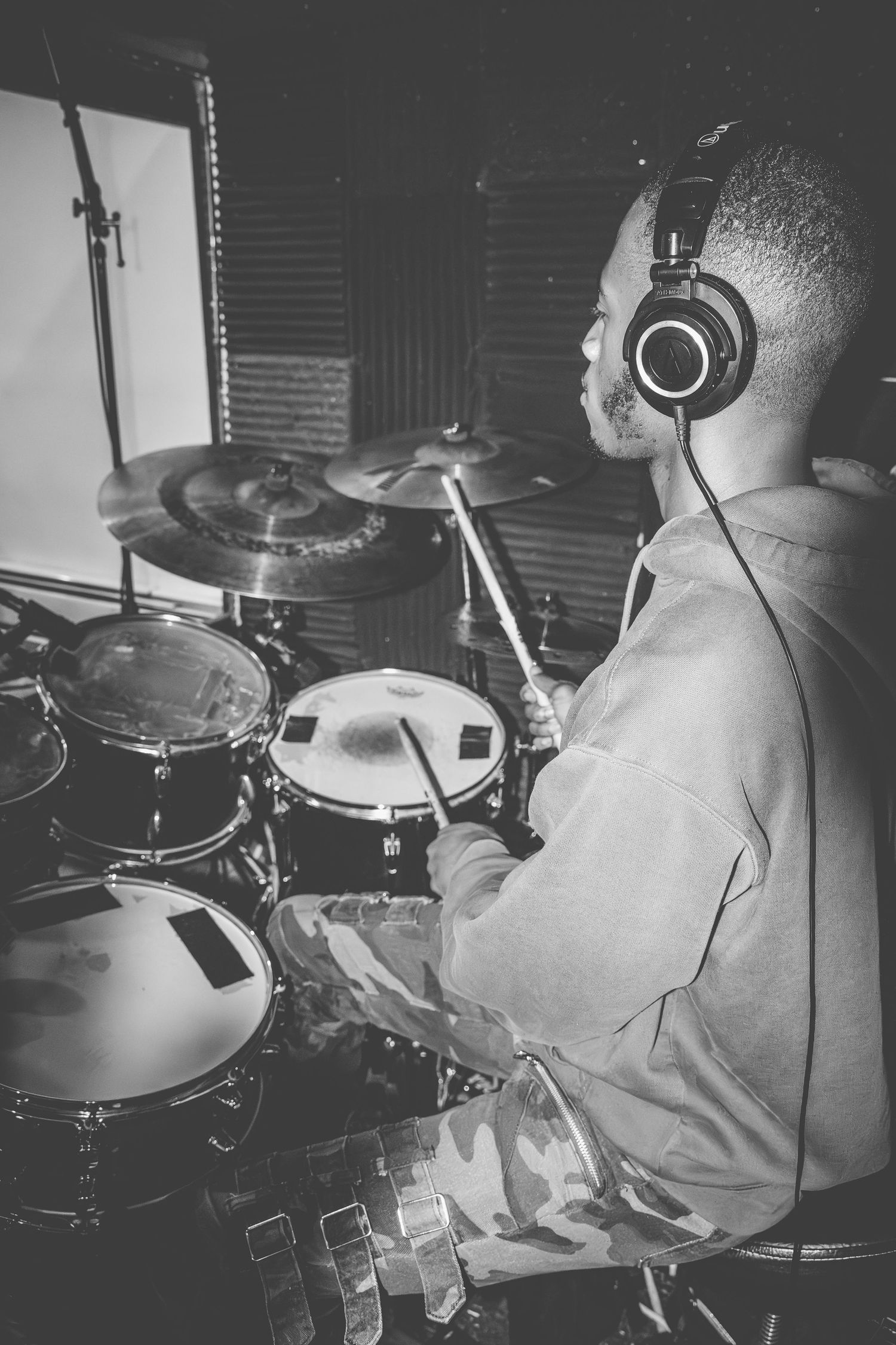 Black and white photos of a drummer performing at a drum kit in a recording studio setting.