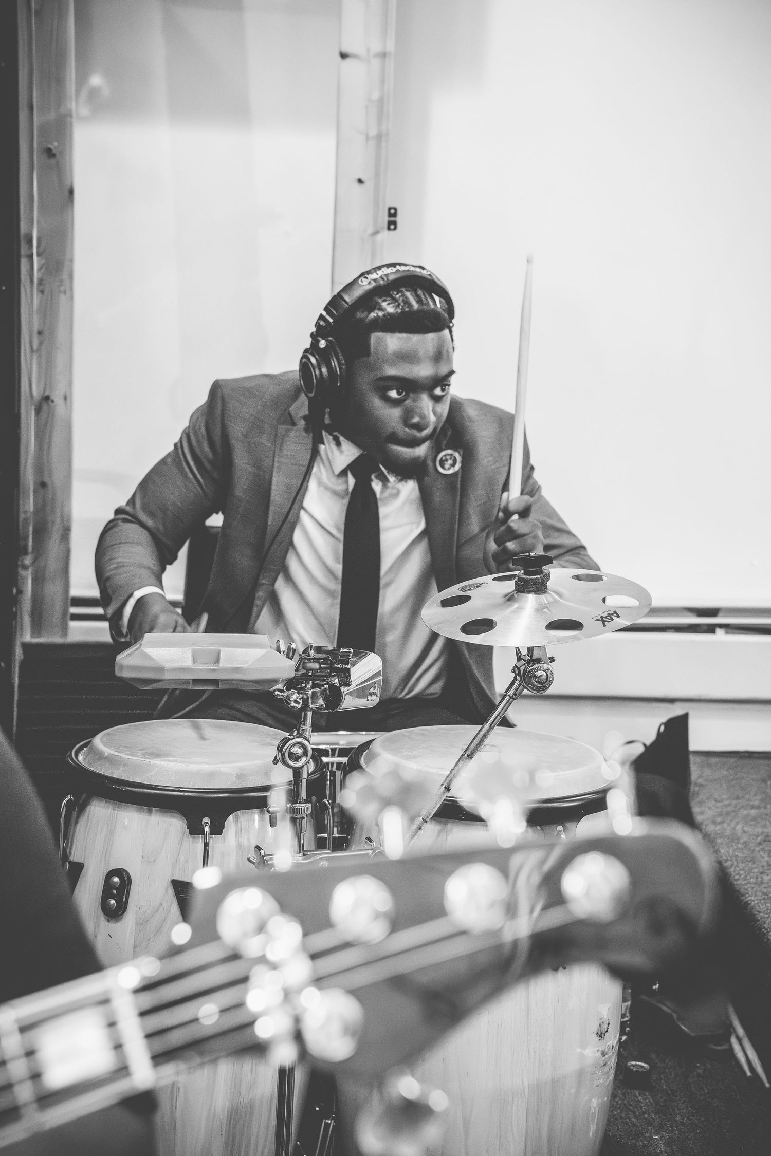Professional musician in a suit plays drums with intense focus in black and white studio photograph.