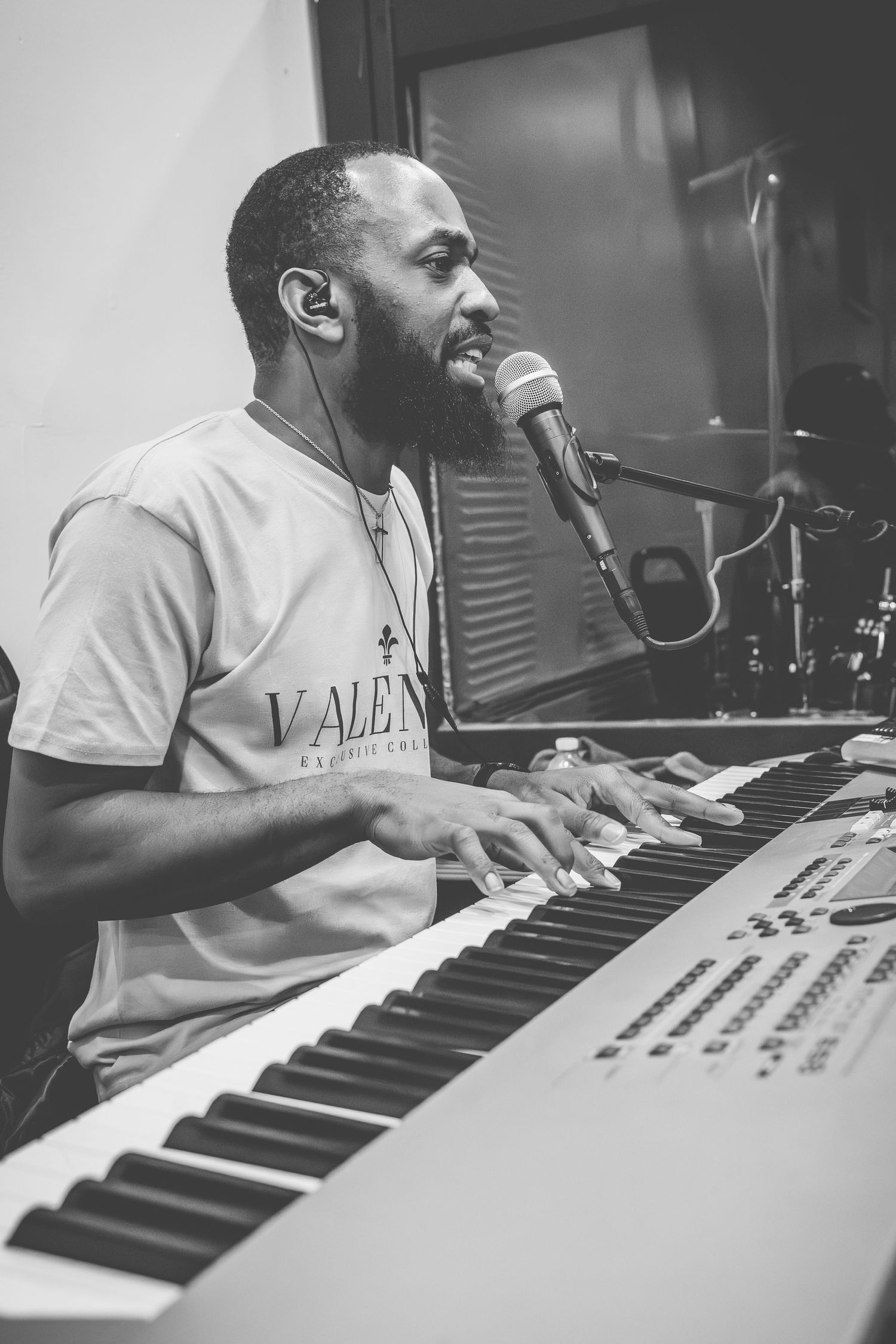 Musician plays keyboard while singing with joyful expression in monochrome studio setting.