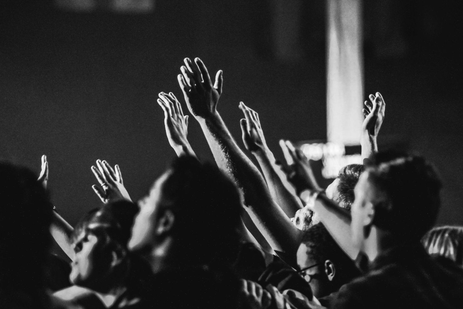Silhouettes of raised hands during a concert or worship service against dark background.