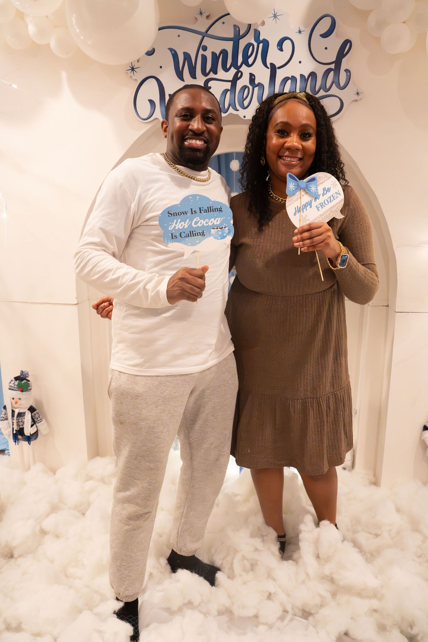 A couple poses playfully in a winter wonderland themed photoshoot with white cotton snow decorations.