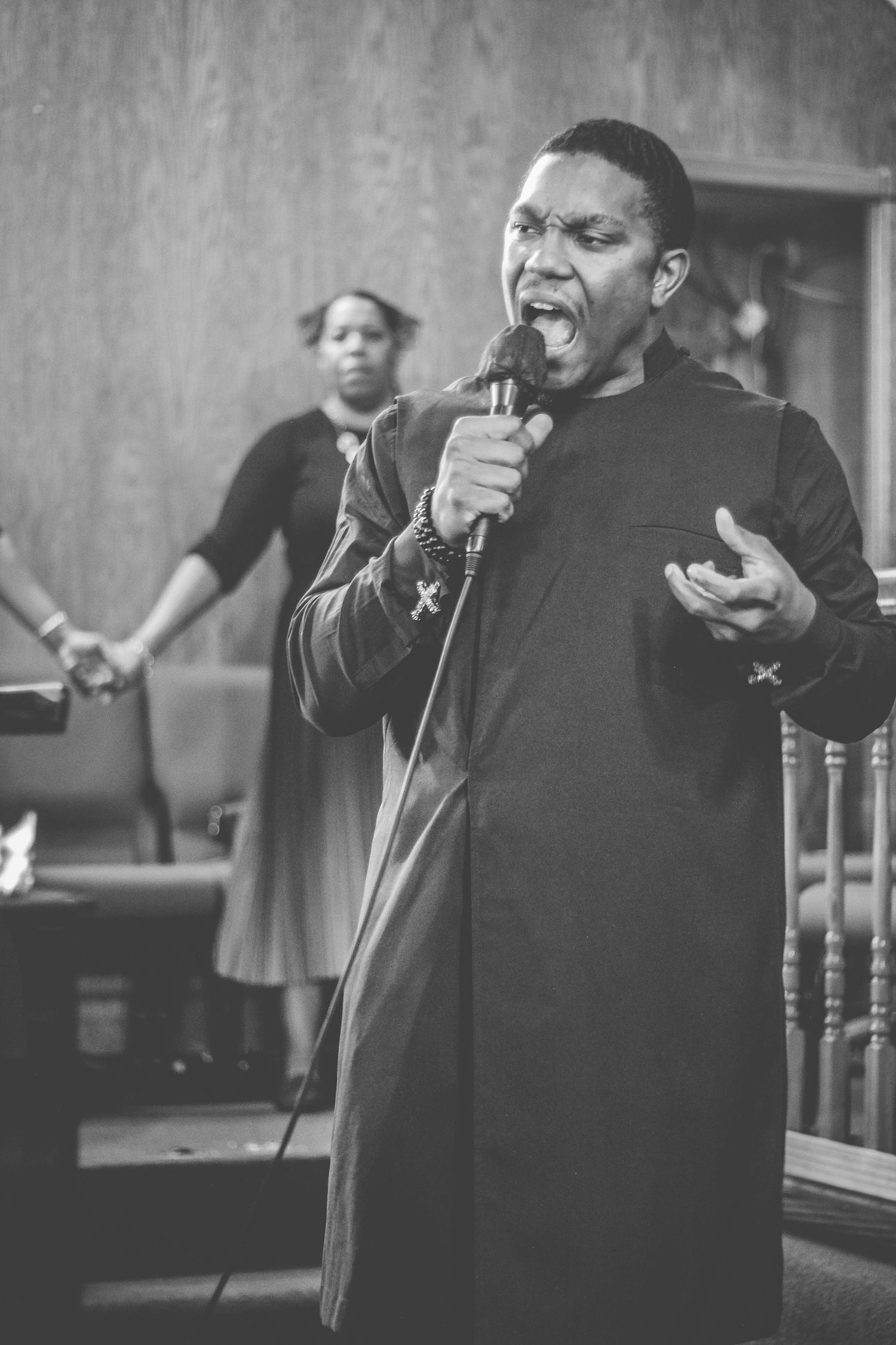 A passionate vocalist performs with a microphone in a black robe during a church service.