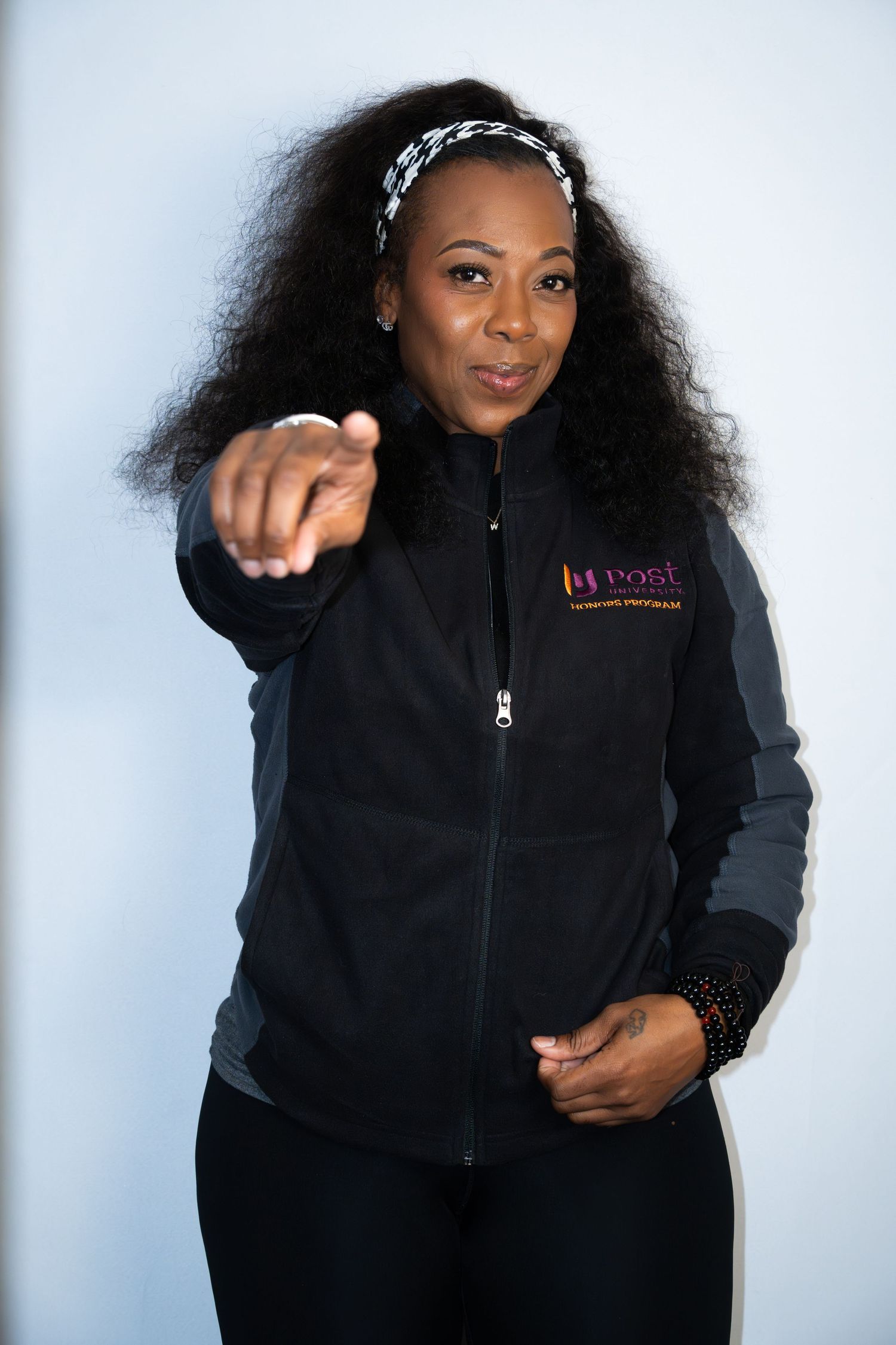 A professional portrait in a black fleece jacket with a pointing gesture against a white background.