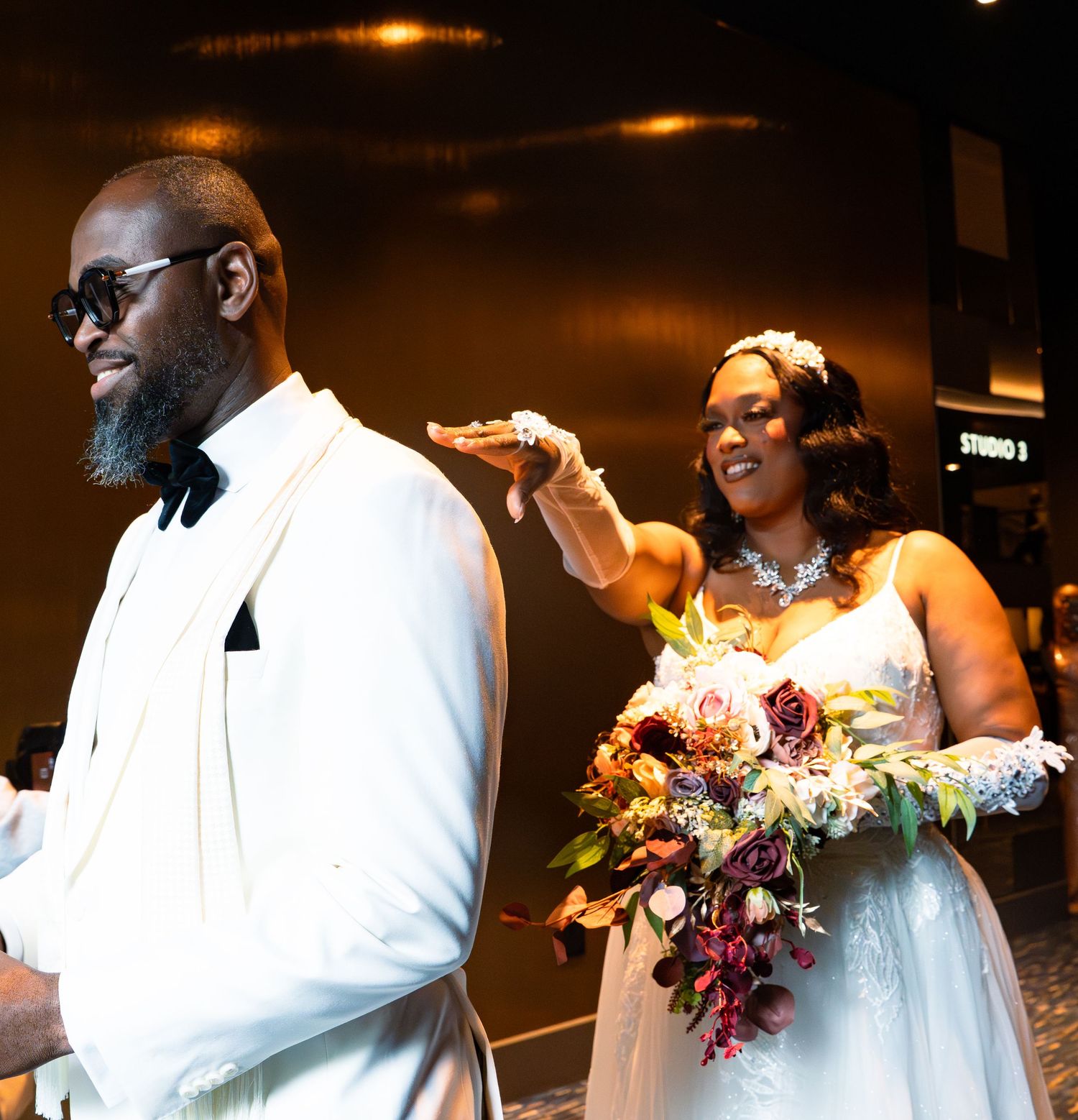 A couple shares a joyful moment during their wedding celebration in a dimly lit venue with floral bouquets.