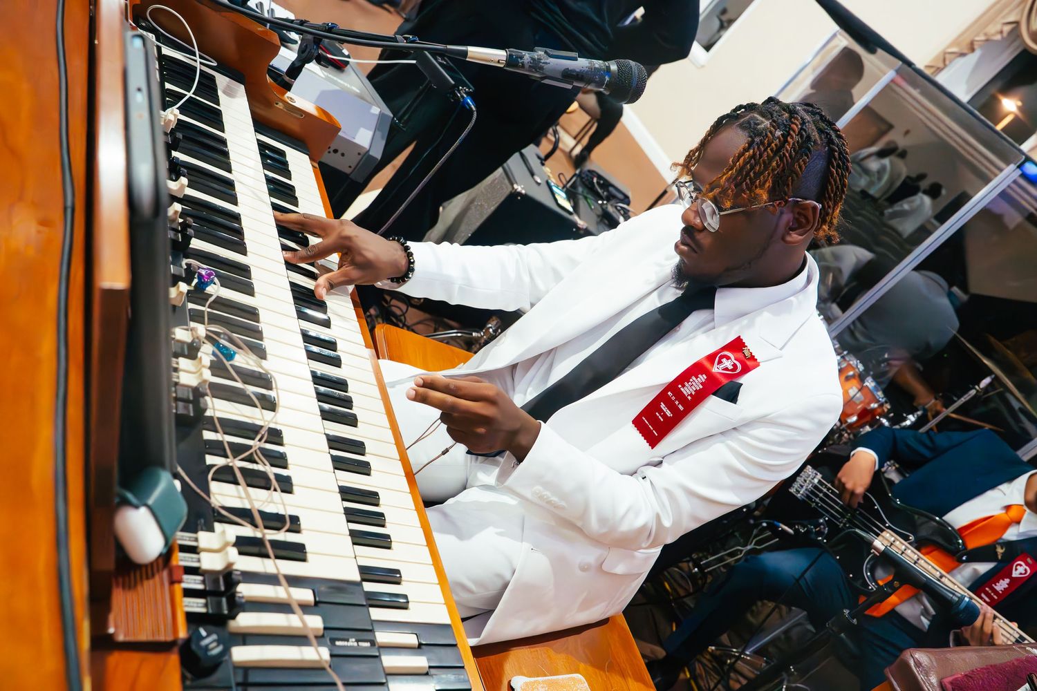 Musicians performing with keyboards and electronic equipment in an orange-tinted setting.
