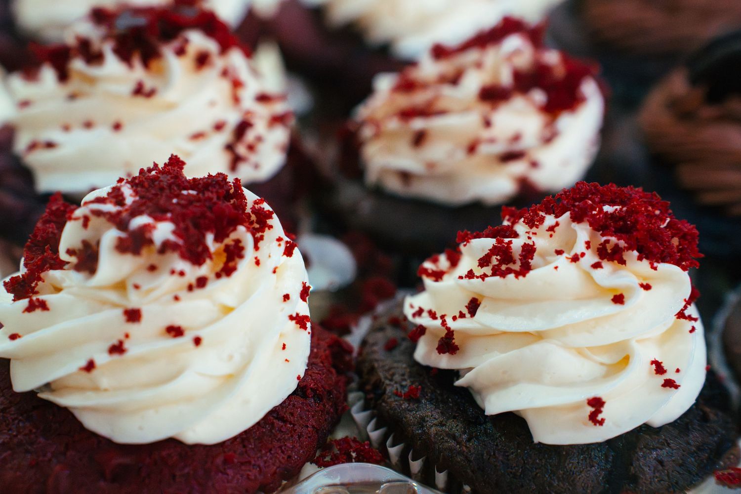 Red velvet cupcakes topped with swirled white cream cheese frosting and red velvet cake crumbs.