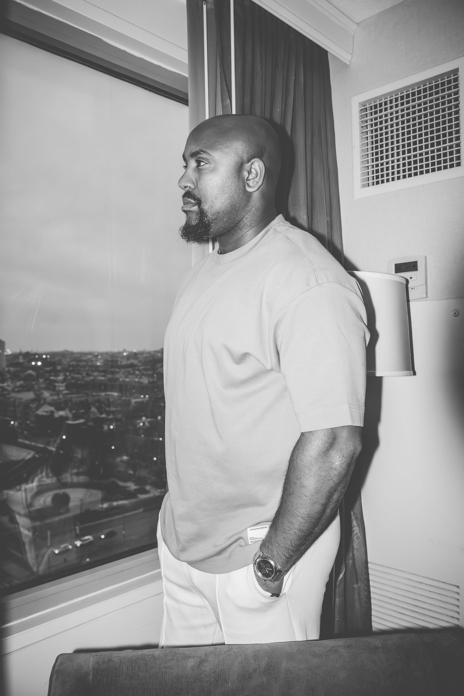 Black and white photos of someone looking out a high-rise window with city views in the background.