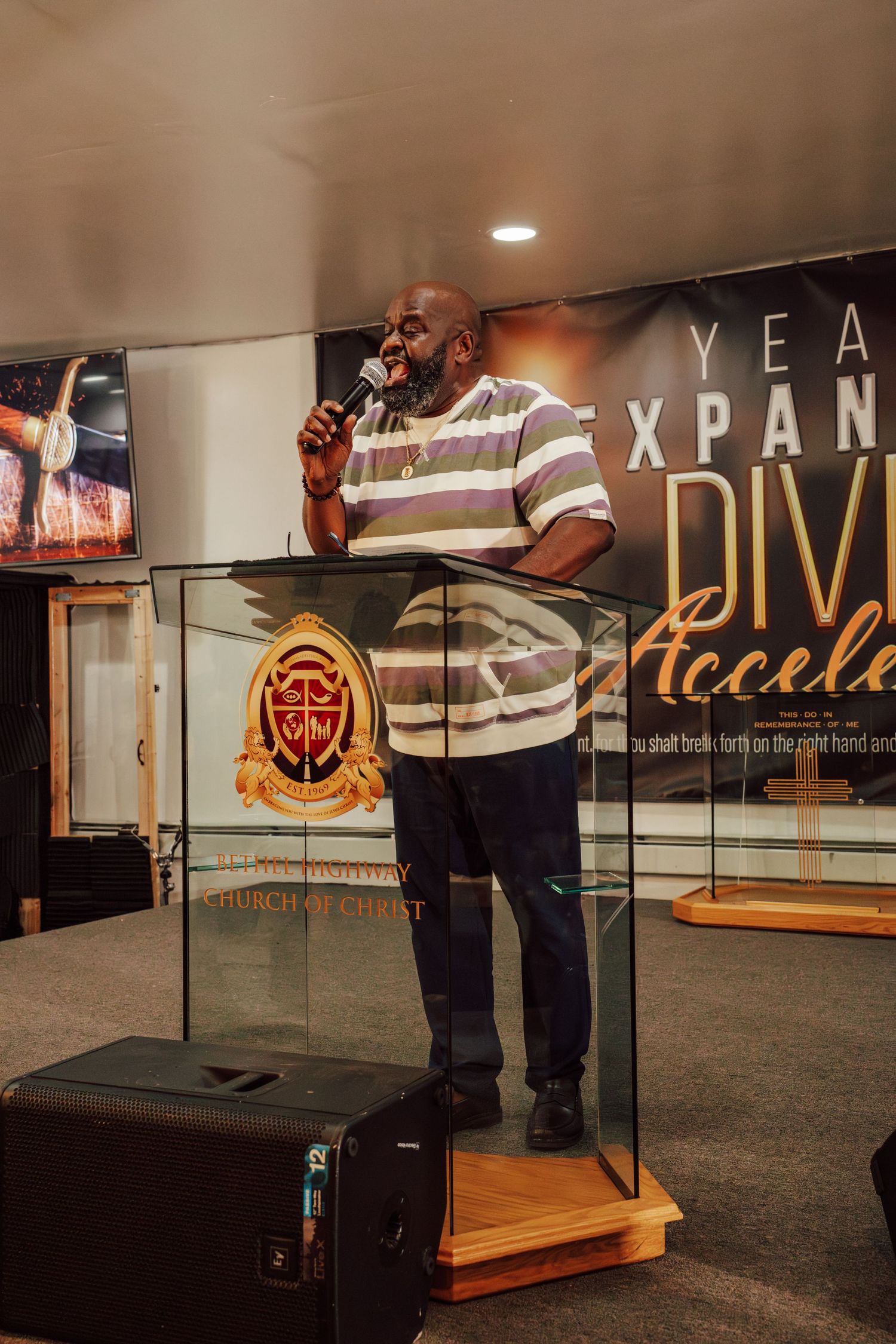 A speaker stands at a podium with a striped polo shirt in front of a church banner.