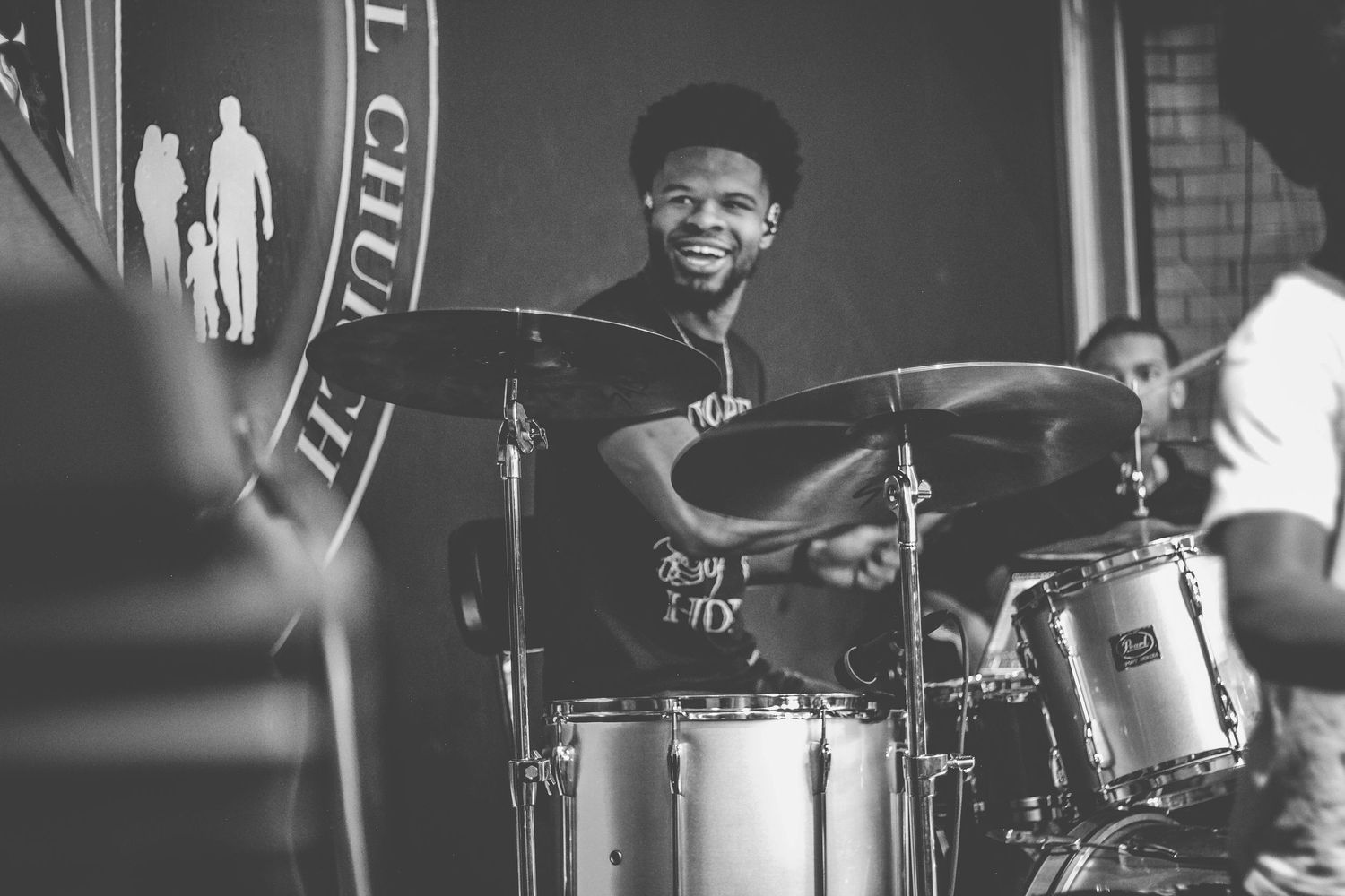 Drummer performing on stage with cymbals and drum kit in monochrome lighting.