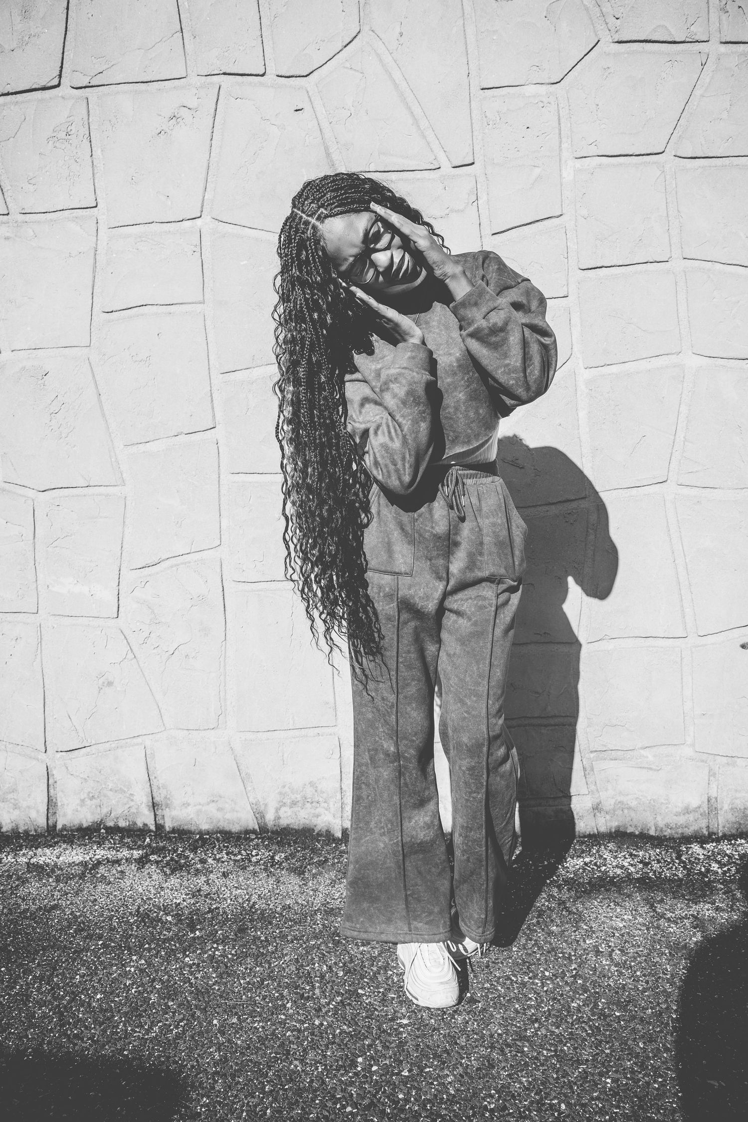 A black and white photo of someone in casual attire posing against a textured wall.