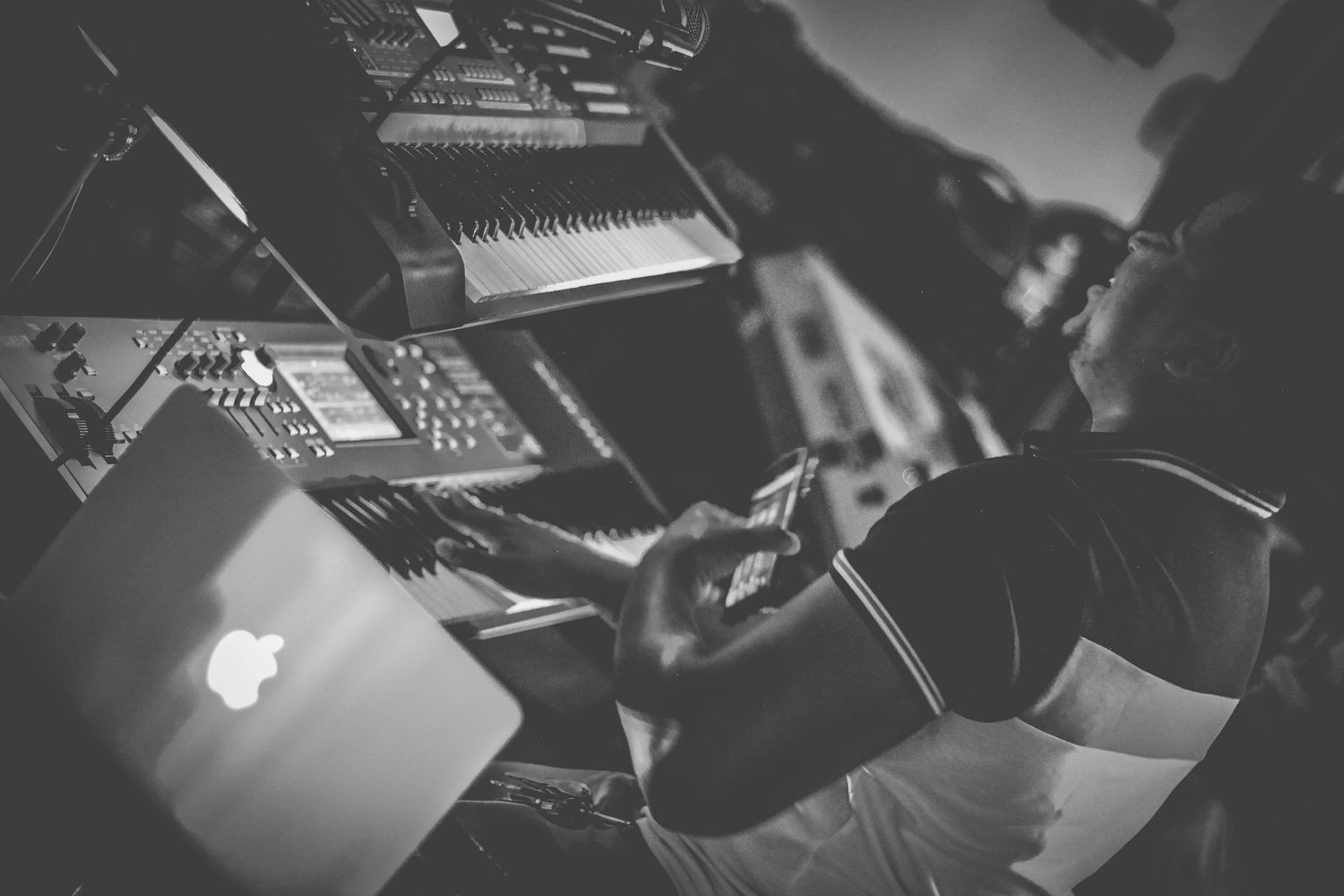 Music producer working in dark studio with laptop and electronic equipment in black and white photo.