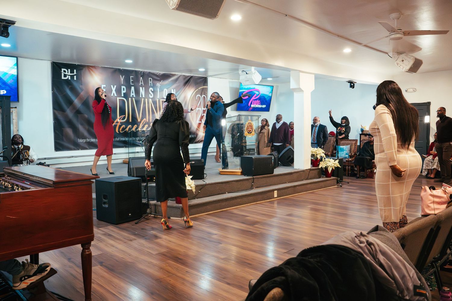 People waiting in a modern dance studio hallway with wooden floors and white walls under bright lighting.