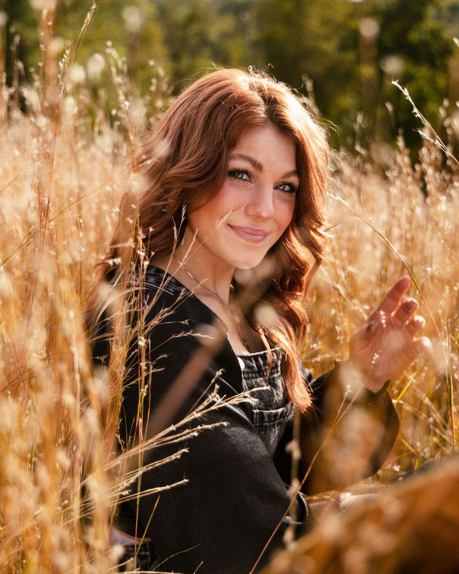 Beautiful redhead woman smiles warmly surrounded by golden tall grass in sunlit field.