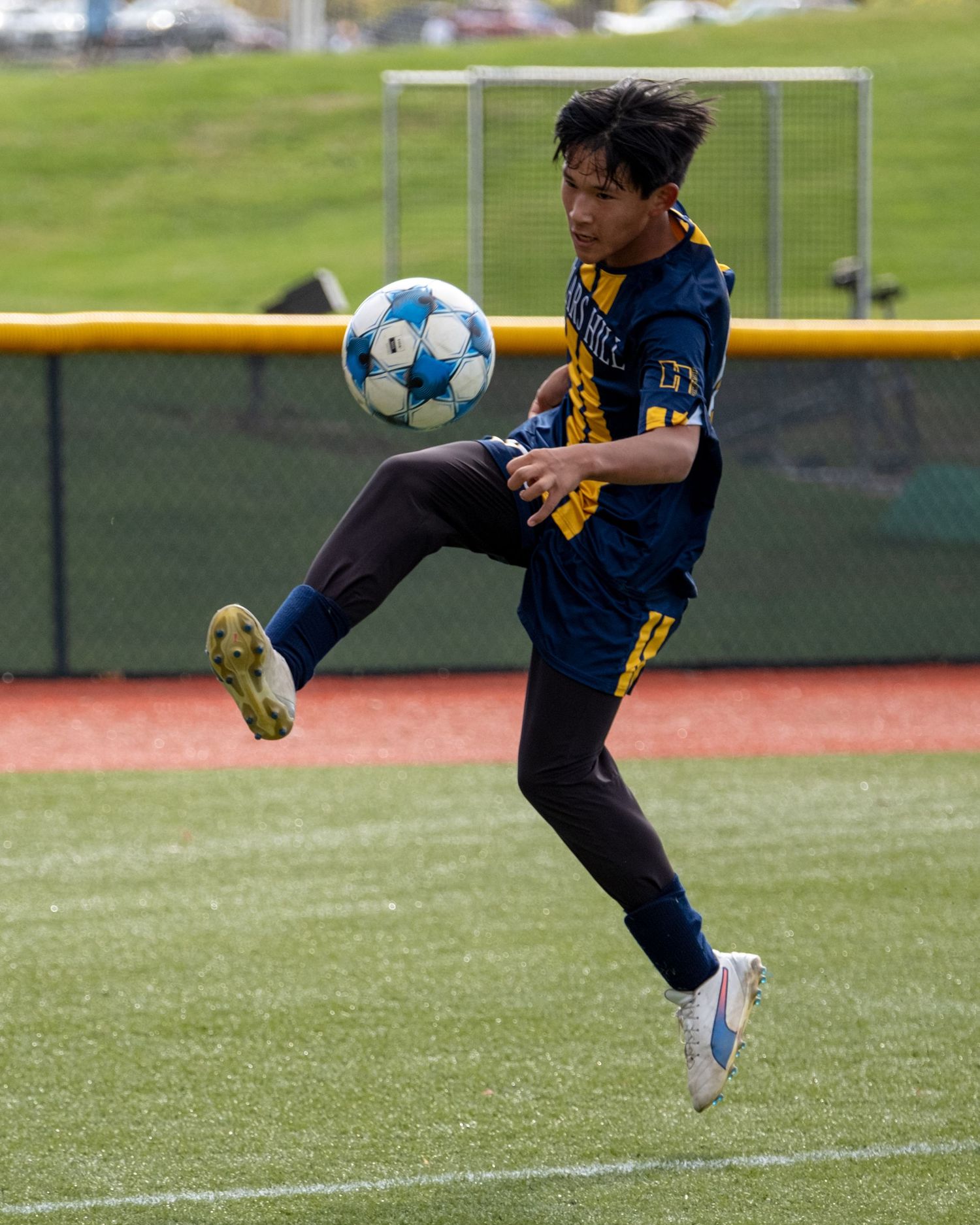 Soccer player in navy uniform skillfully controlling ball mid-air on green field.