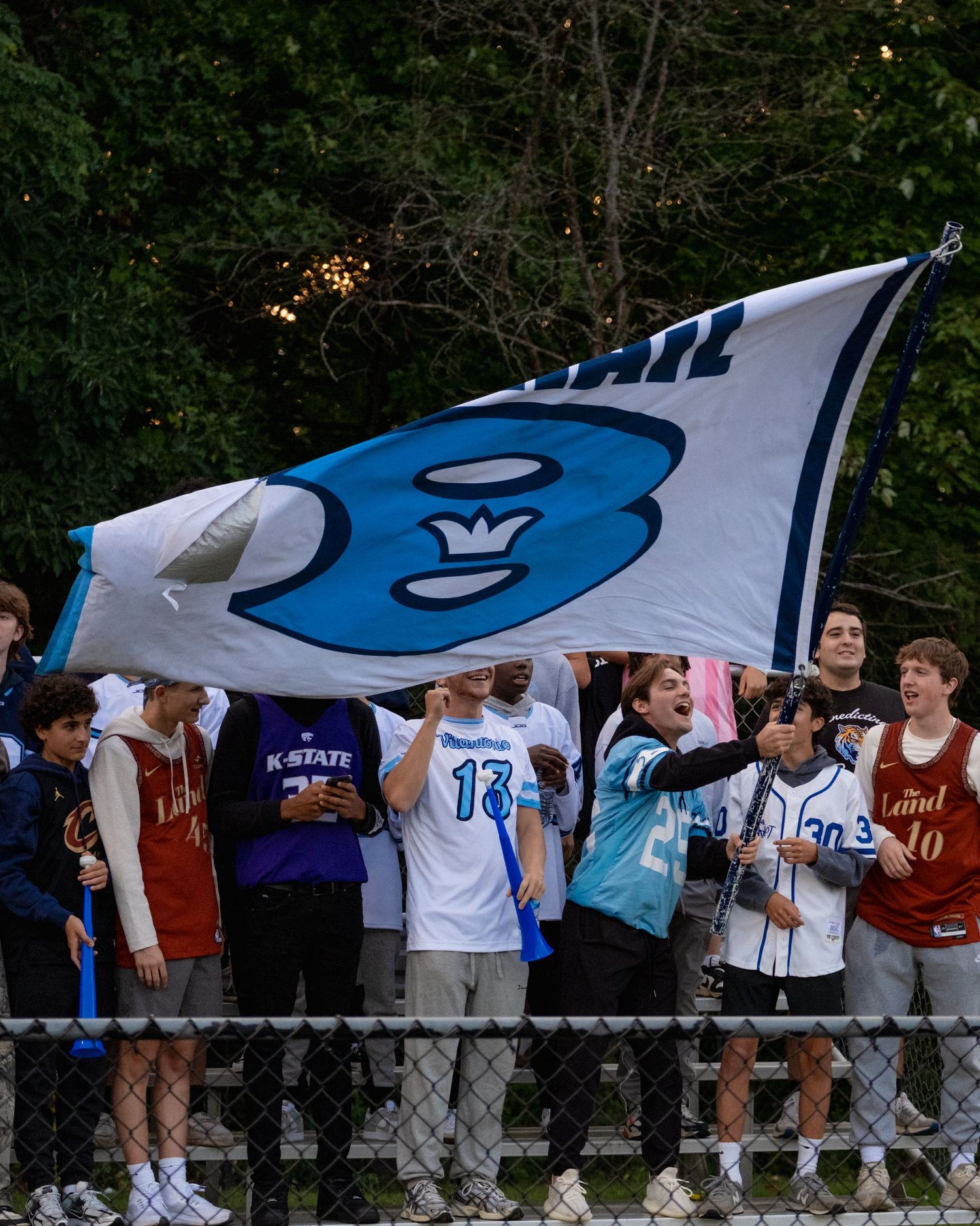 Fans wave a large Benedictine logo flag in the stands during a football game.