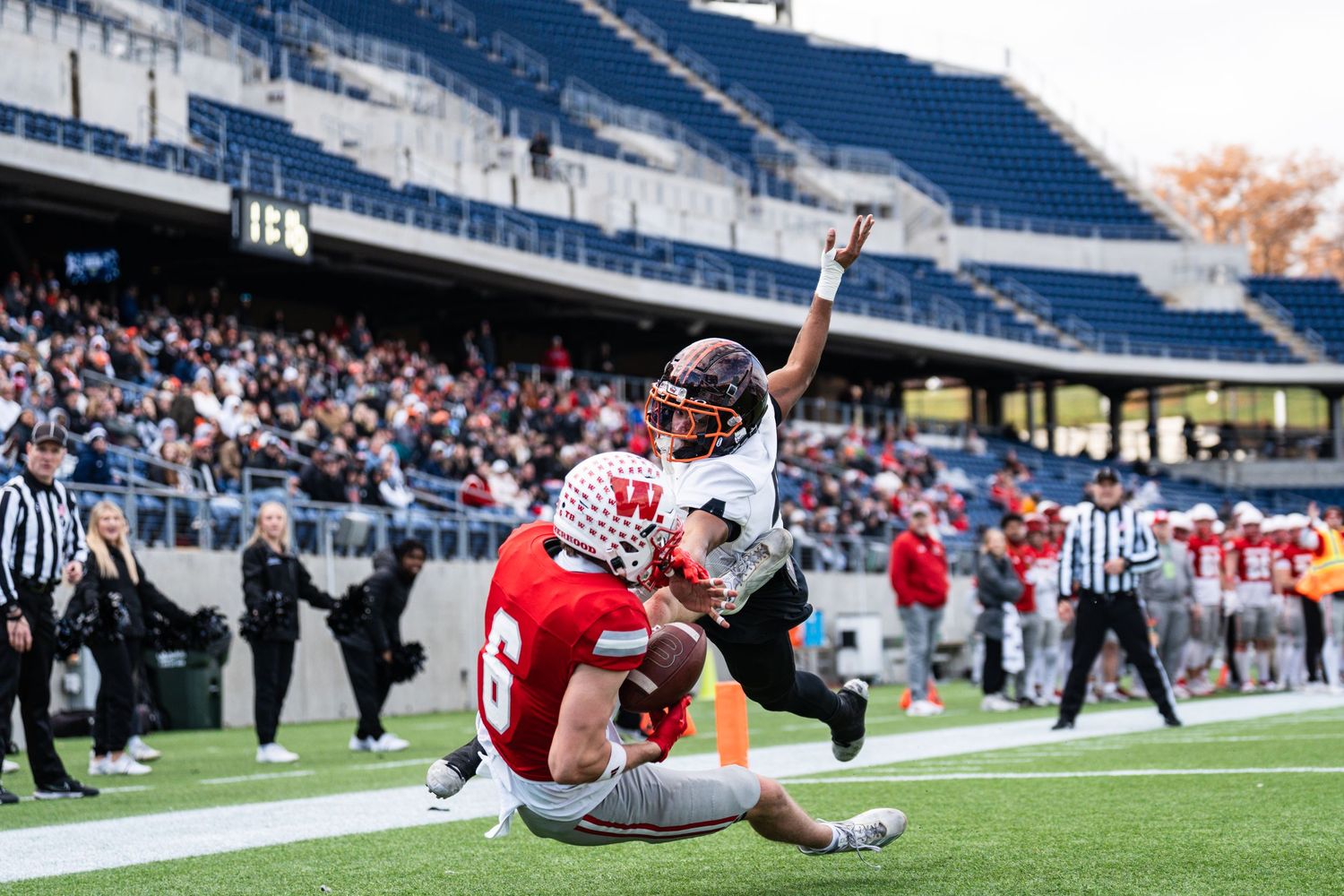 Football player in black uniform scores touchdown while being tackled in packed stadium.