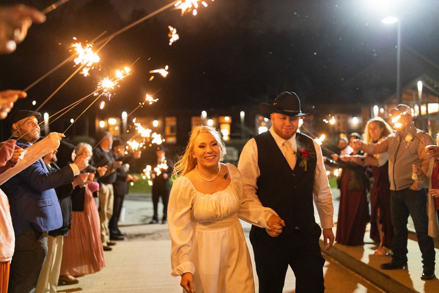 Bride and groom walking through a sparkler send-off tunnel during their outdoor nighttime wedding exit.
