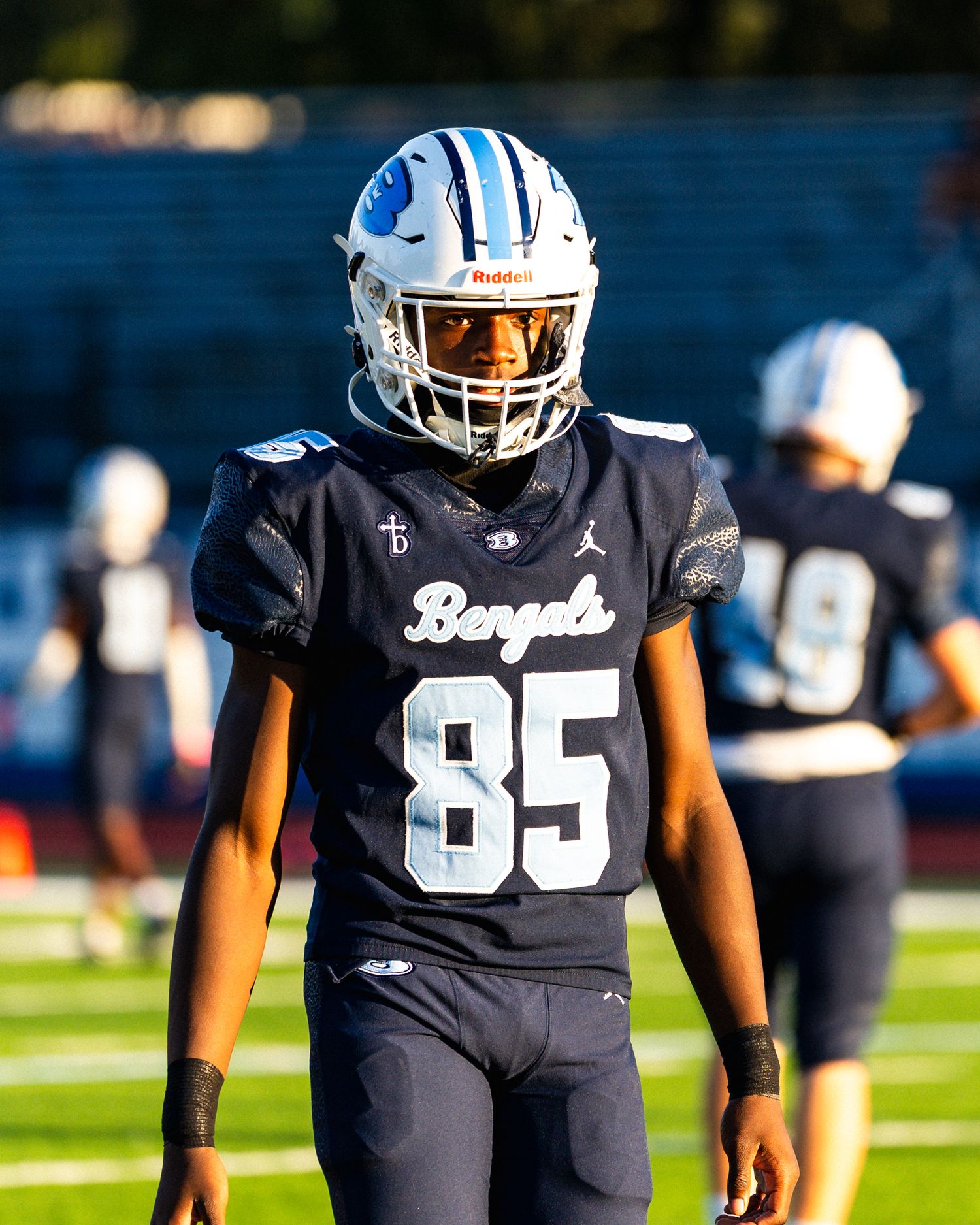 High school football player wearing navy Bengals jersey number 85 stands on field before game.