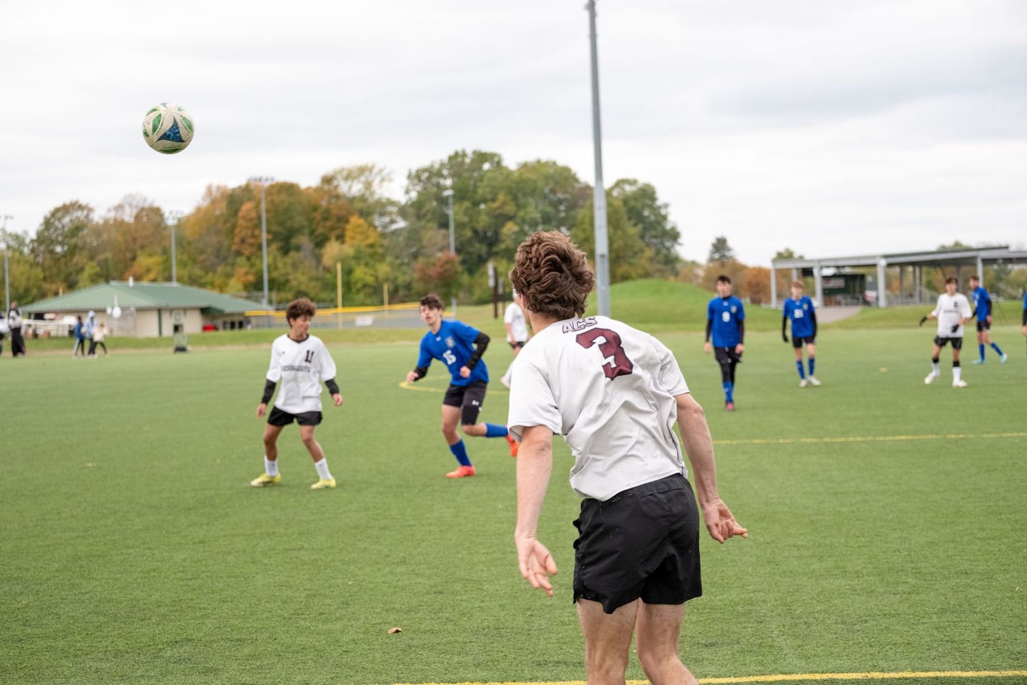 Youth soccer players compete on a green field with number 3 preparing to head the ball.