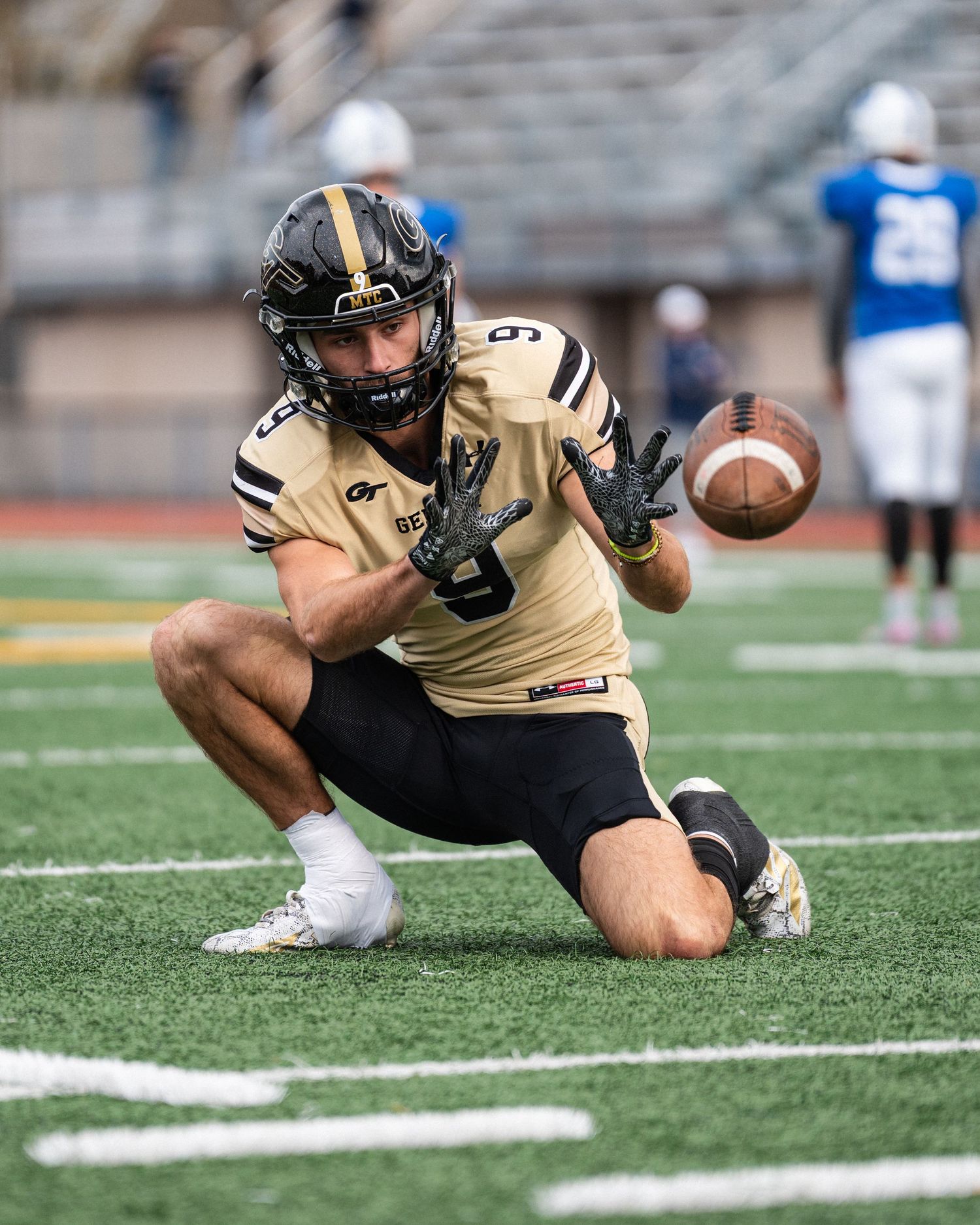 Football player in black and gold uniform catches a pass during a game on a turf field.