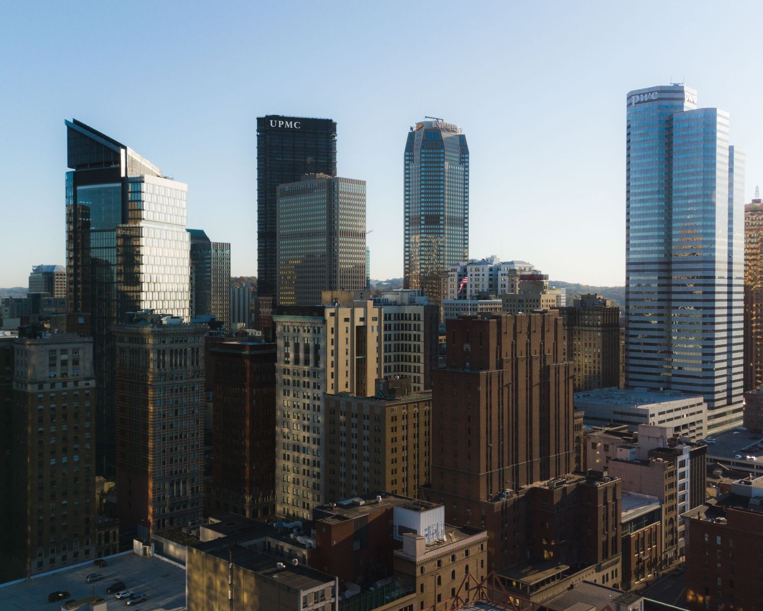 Daytime aerial view of Pittsburgh downtown skyline with PNC and modern glass skyscrapers under blue sky.
