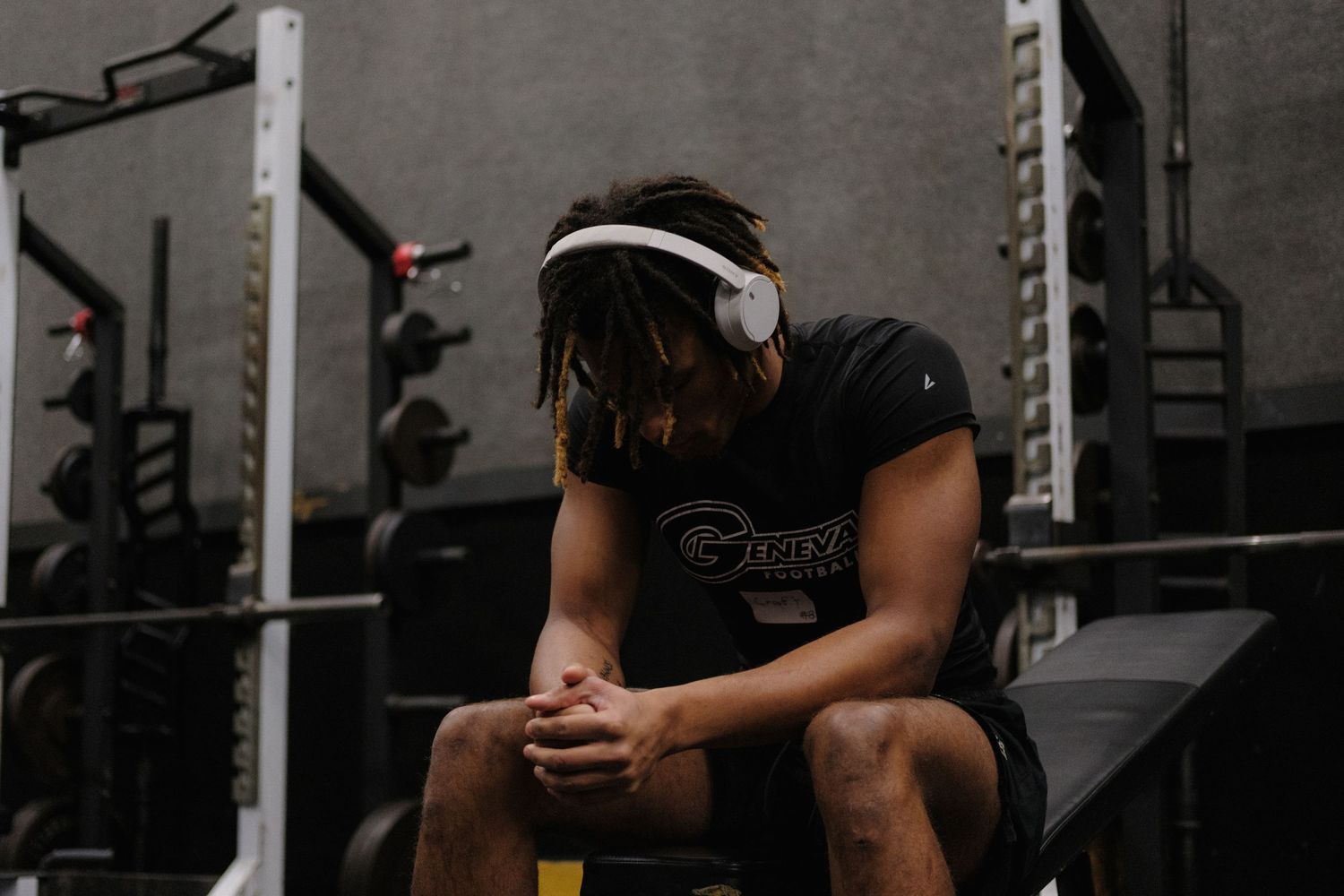 Male athlete with headphones sitting and resting in a gym between workout sets.