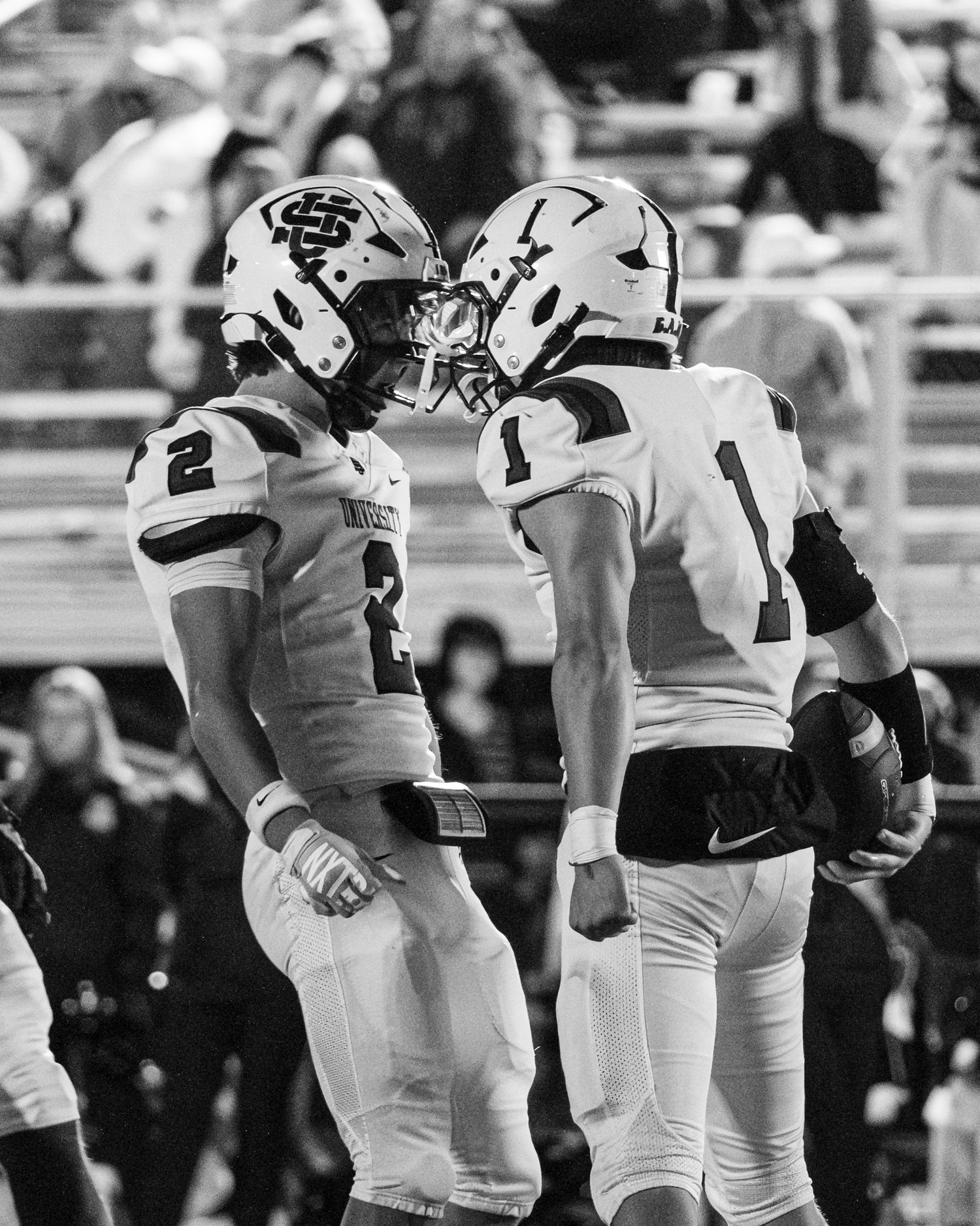 Two University football players touching helmets in black and white game photo.