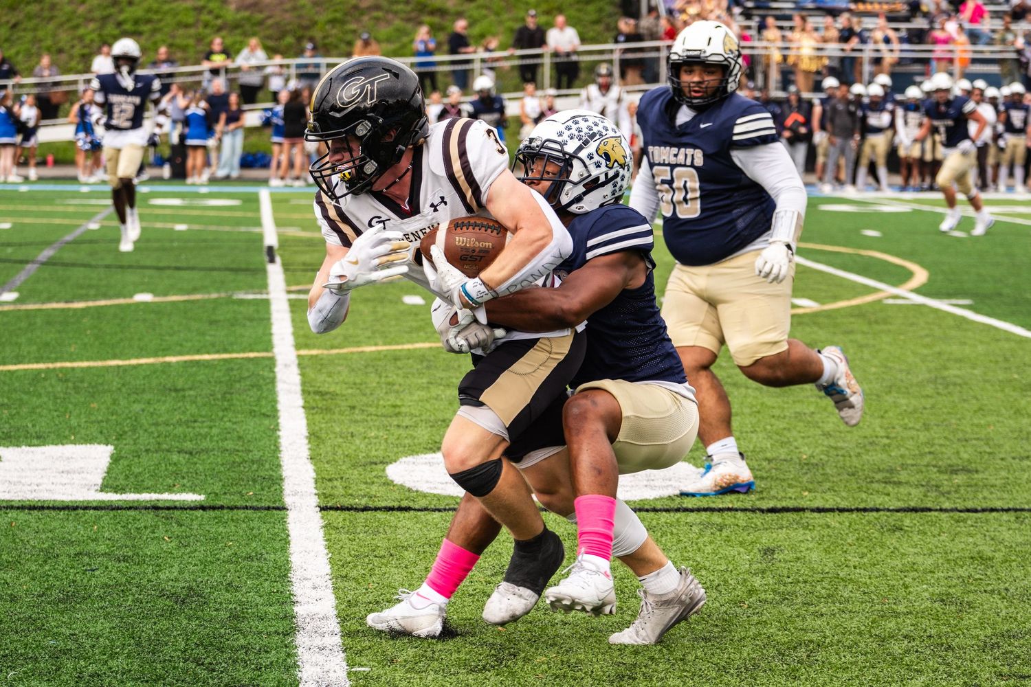 Football players tackle ball carrier during daytime game.
