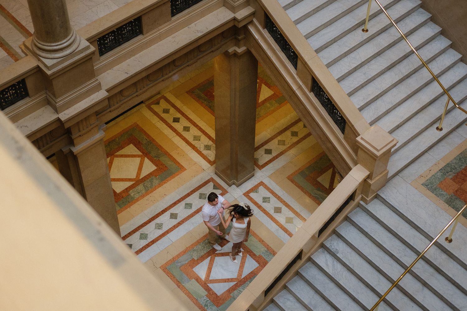 Aerial view of couple standing together on ornate tiled floor of grand classical building.